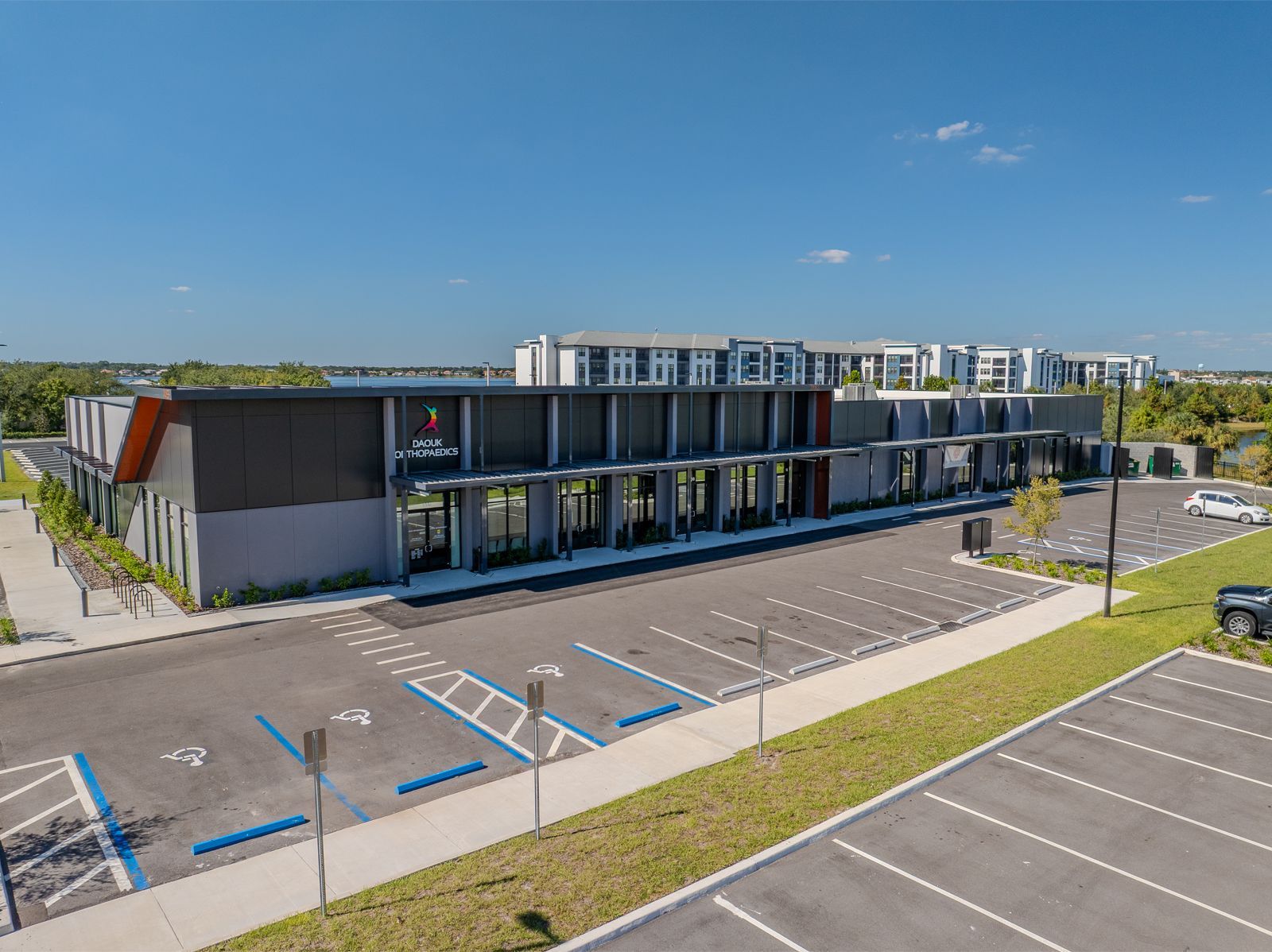 An aerial view of a modern building with a large parking lot. Blue handicap parking spaces are visible.