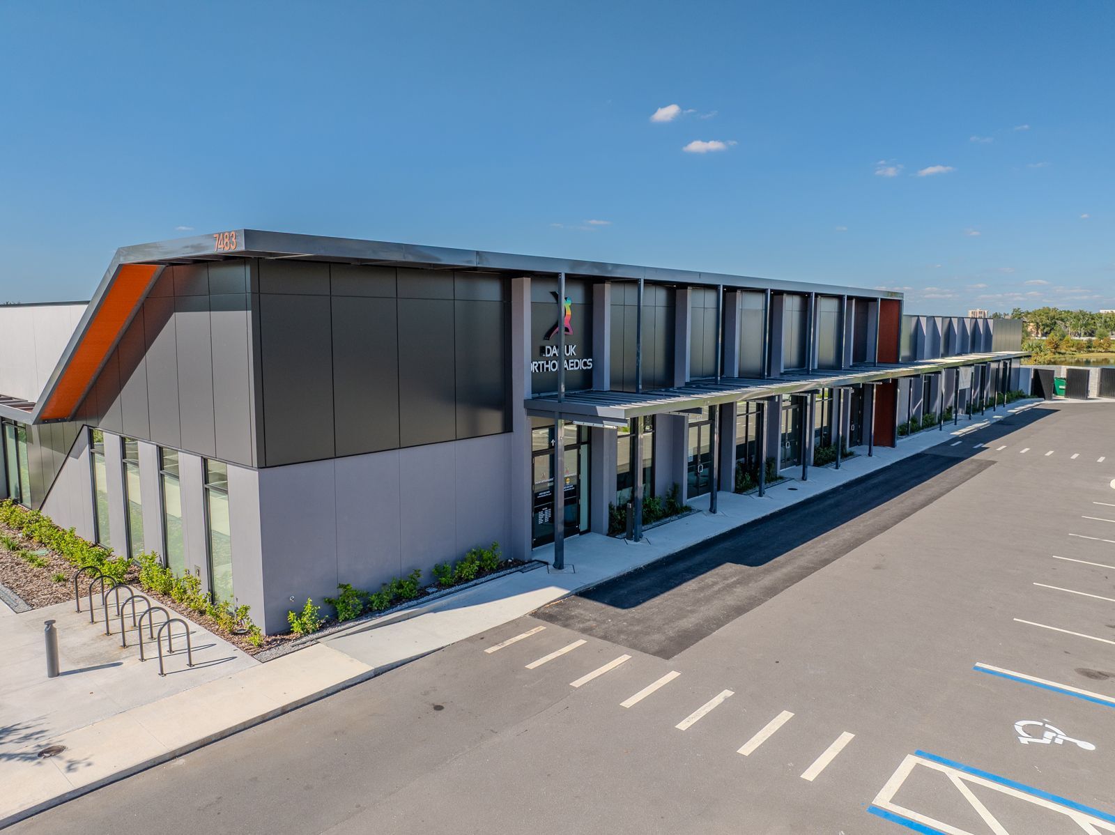 Modern gray and black building with large windows and a parking lot.