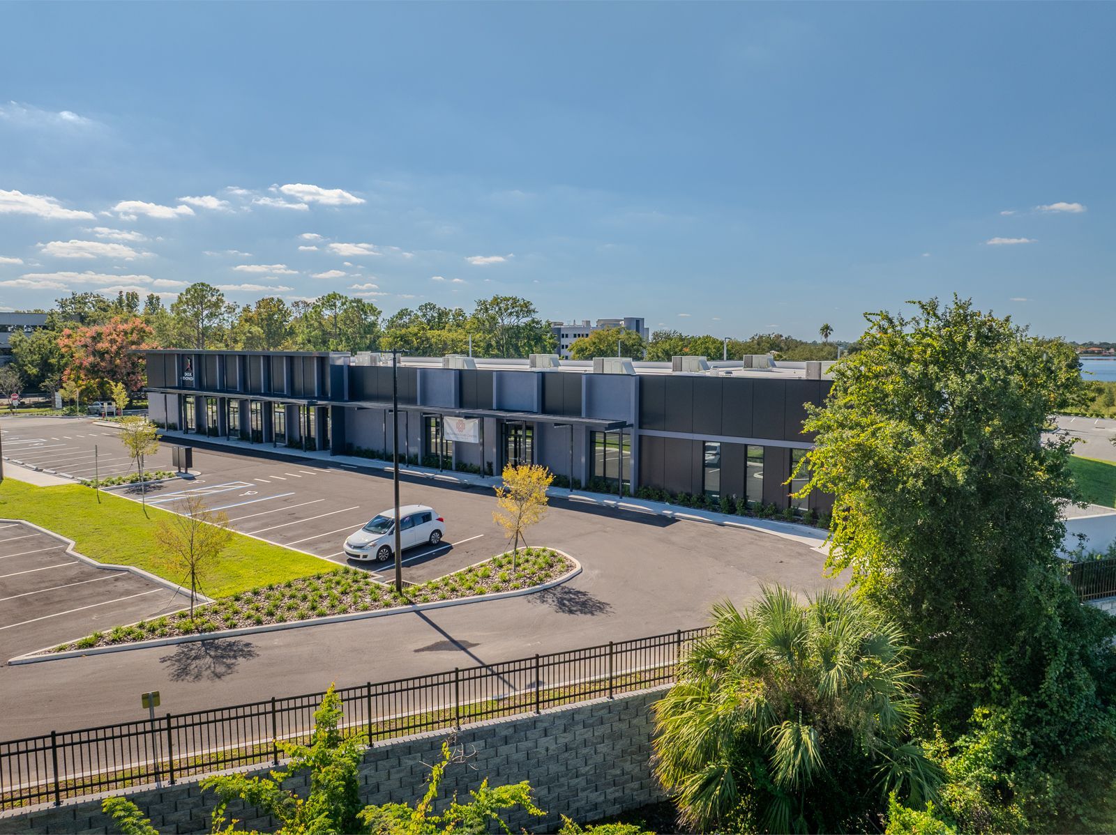 Modern commercial building with parking lot under a blue sky; a car is parked out front.