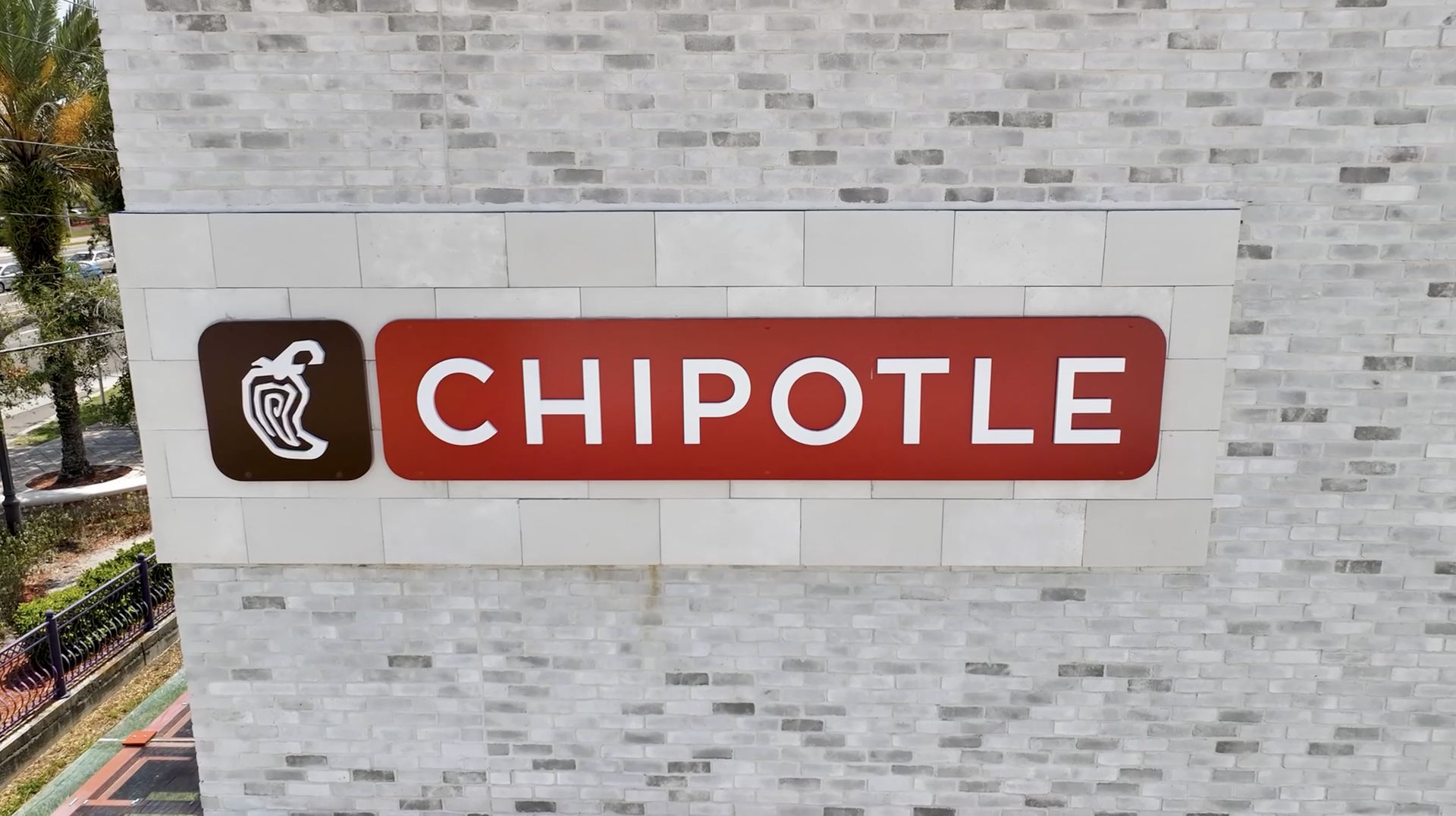 Chipotle restaurant sign with a red and white logo on a gray brick wall.