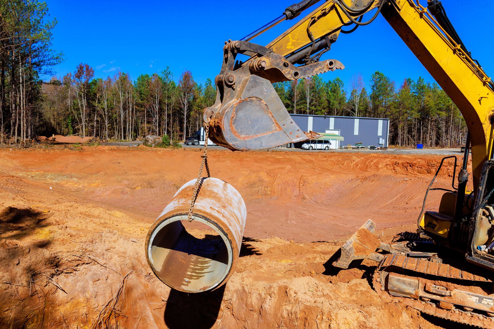 A yellow excavator is lifting a large pipe out of the ground.