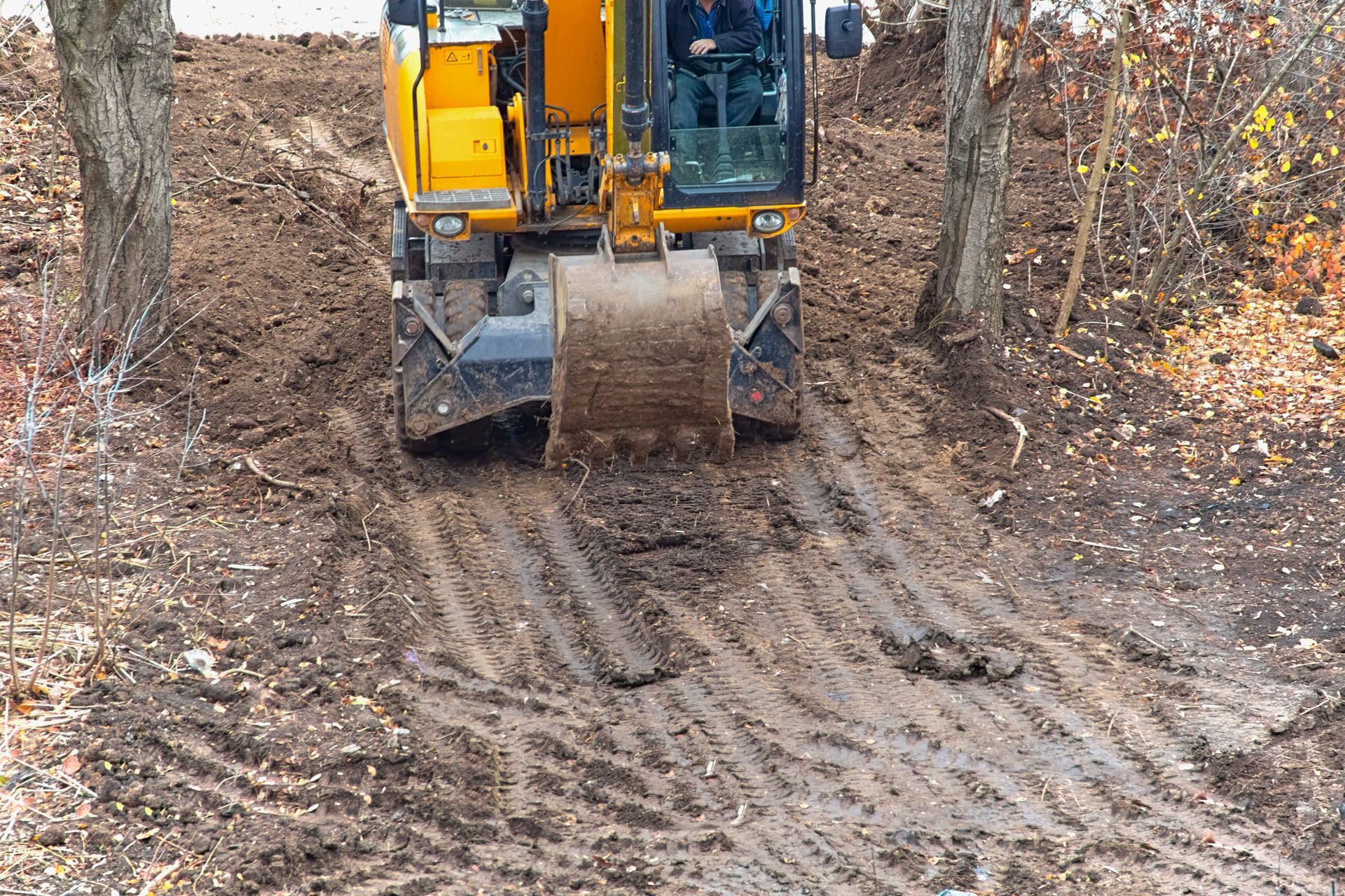 A yellow excavator is driving down a muddy road.