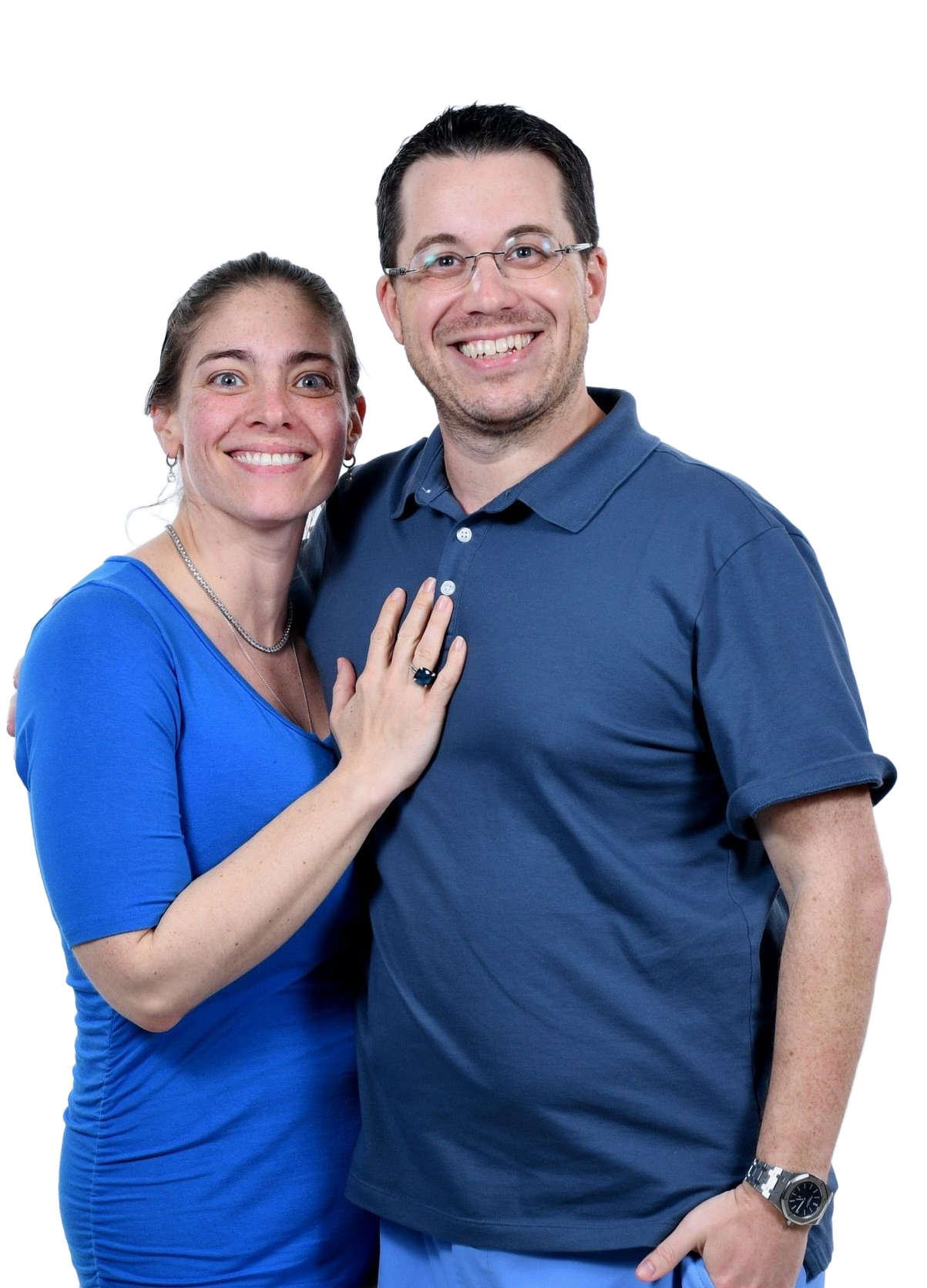 A smiling couple posing against a white background; she wears a blue dress, and he wears a blue polo shirt and glasses.