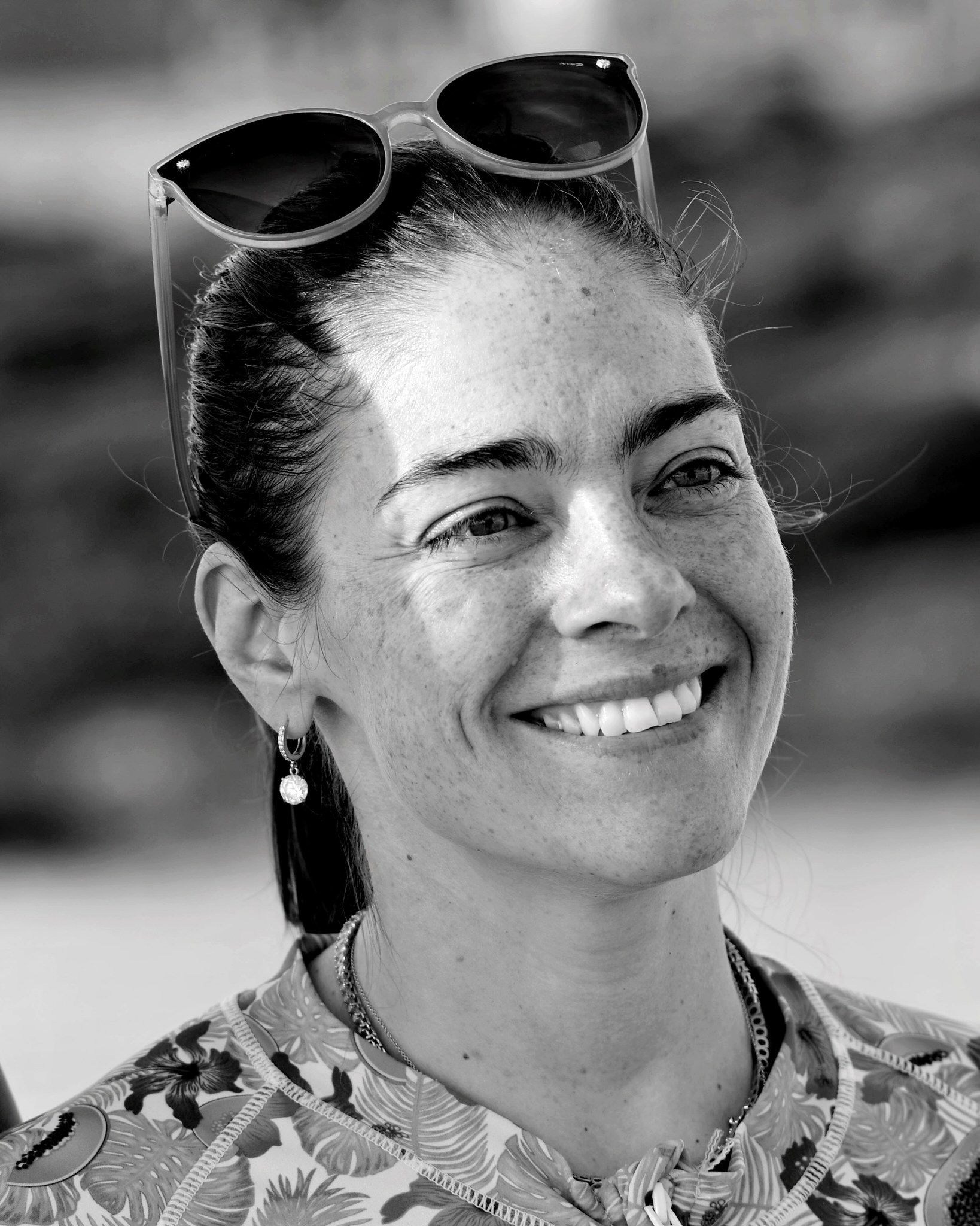A black-and-white headshot of a smiling person with sunglasses resting on top of their head.