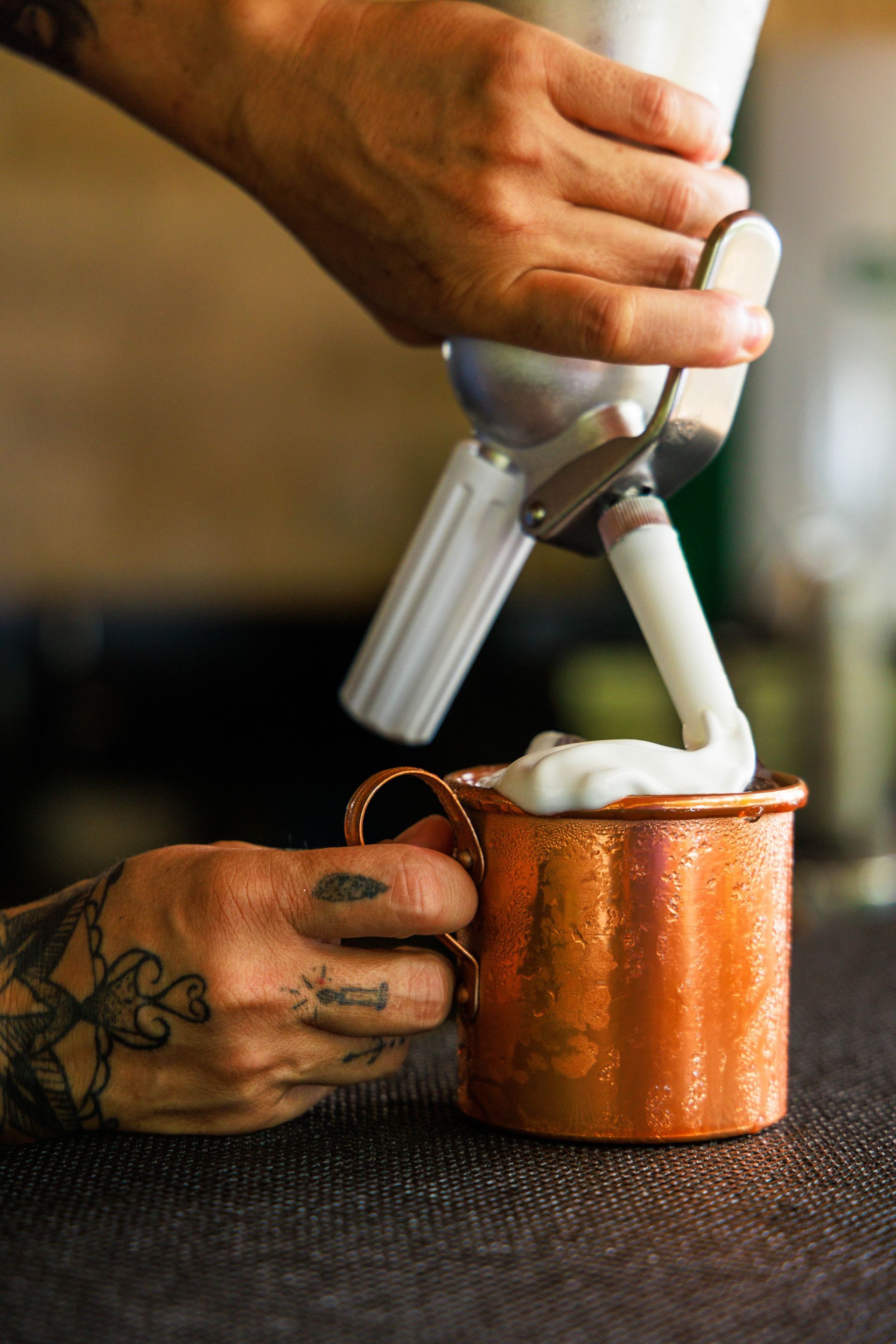 Uma pessoa está despejando chantilly em uma caneca de cobre.