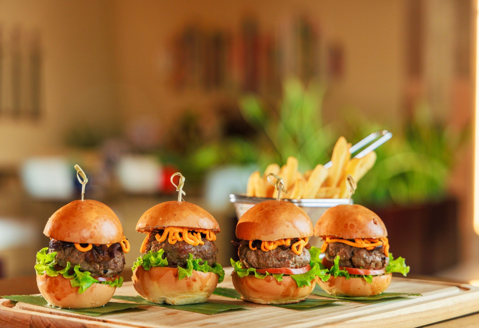 Três hambúrgueres e batatas fritas em uma tábua de corte de madeira.