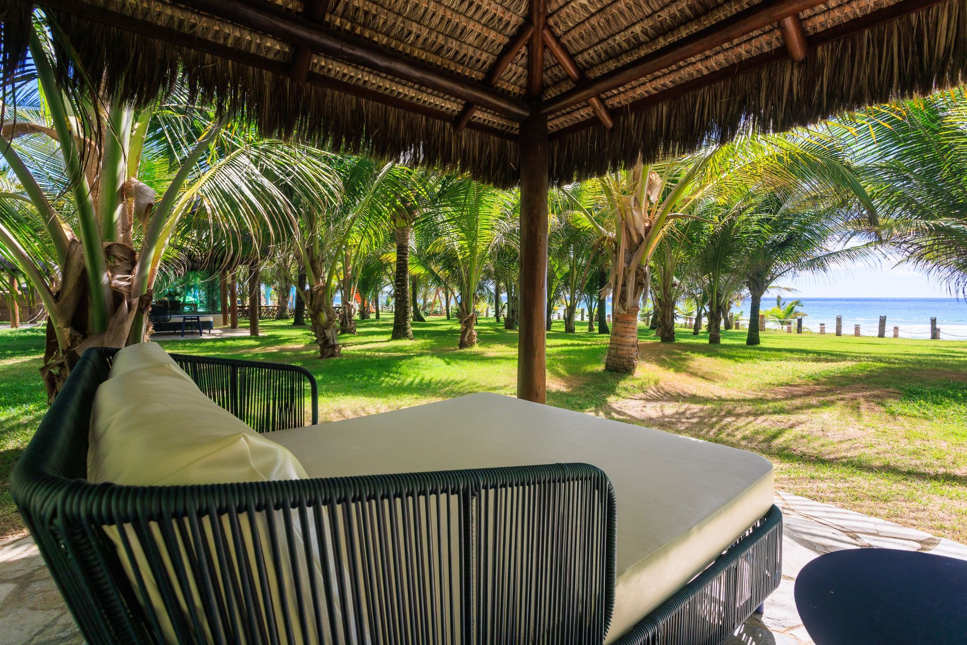 Há uma cama sob um telhado de palha no meio de um campo verdejante.