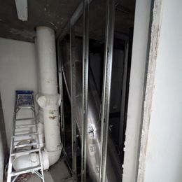 Metal framing around a vertical pipe and ductwork; ladder leaning nearby, construction site.
