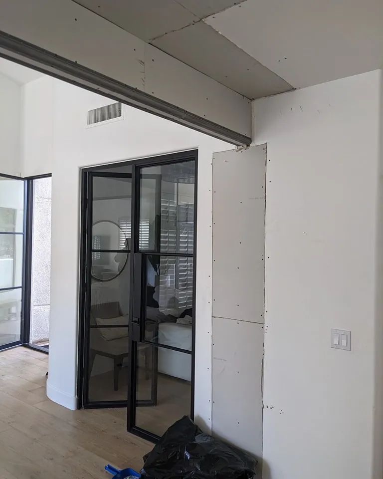 Interior: doorway with black metal frame, partially framed drywall, and white walls, under construction.