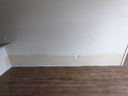 Tan wall with brown wood floor. Electrical outlets, tan lower section, and corner.