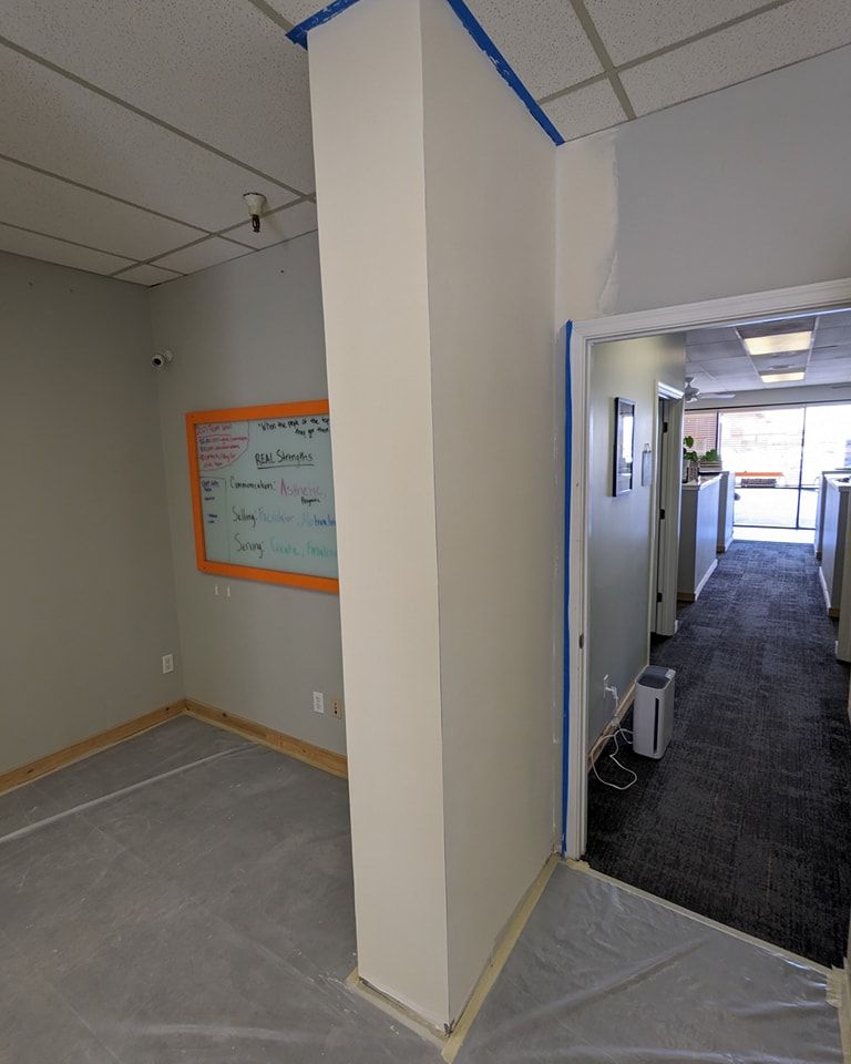 Room being painted with white walls and blue tape. Includes a whiteboard and open doorway.