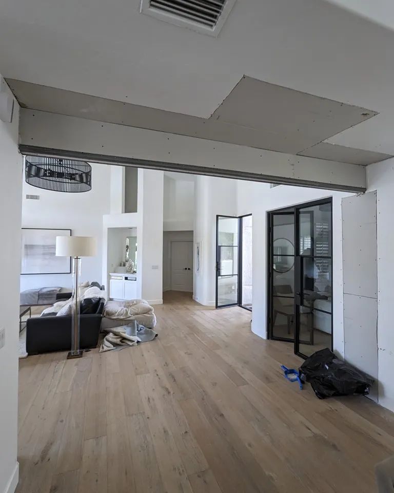 Interior view with wood floors, open doorways, exposed ceiling work, and modern black framed glass doors.