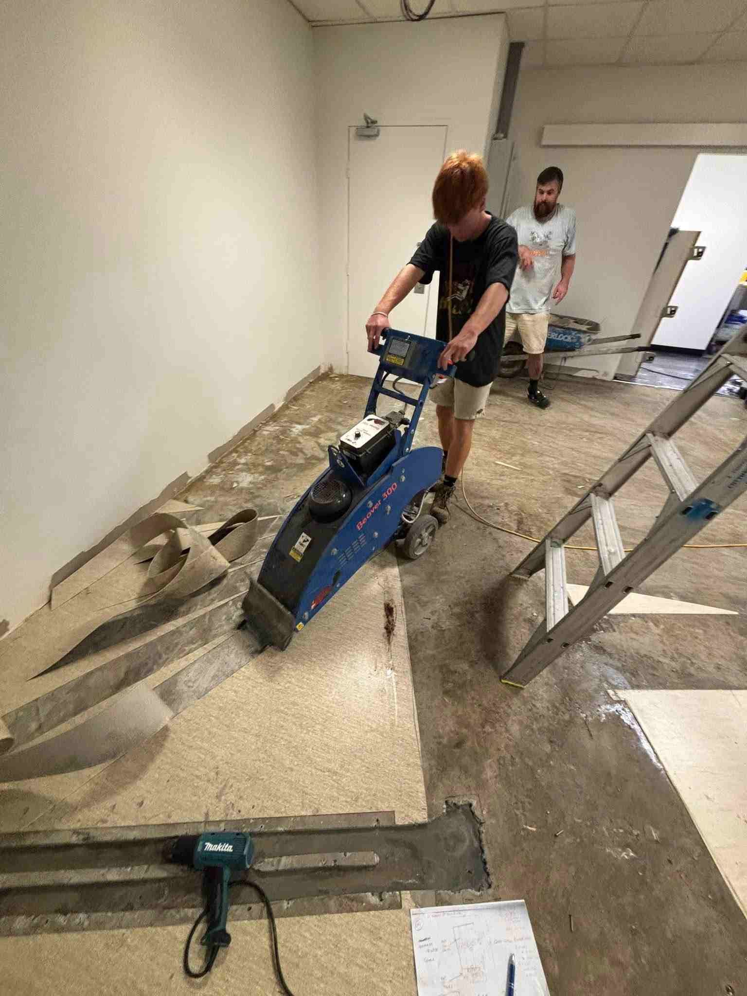 Classroom with rows of desks and blue chairs, neutral-toned speckled flooring.