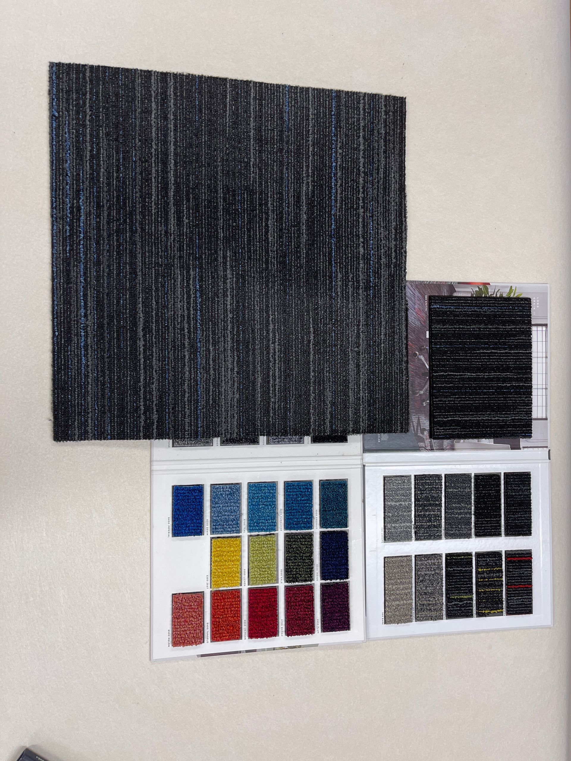 Carpet samples in various colors and textures, with a large square of black and gray striped carpet.
