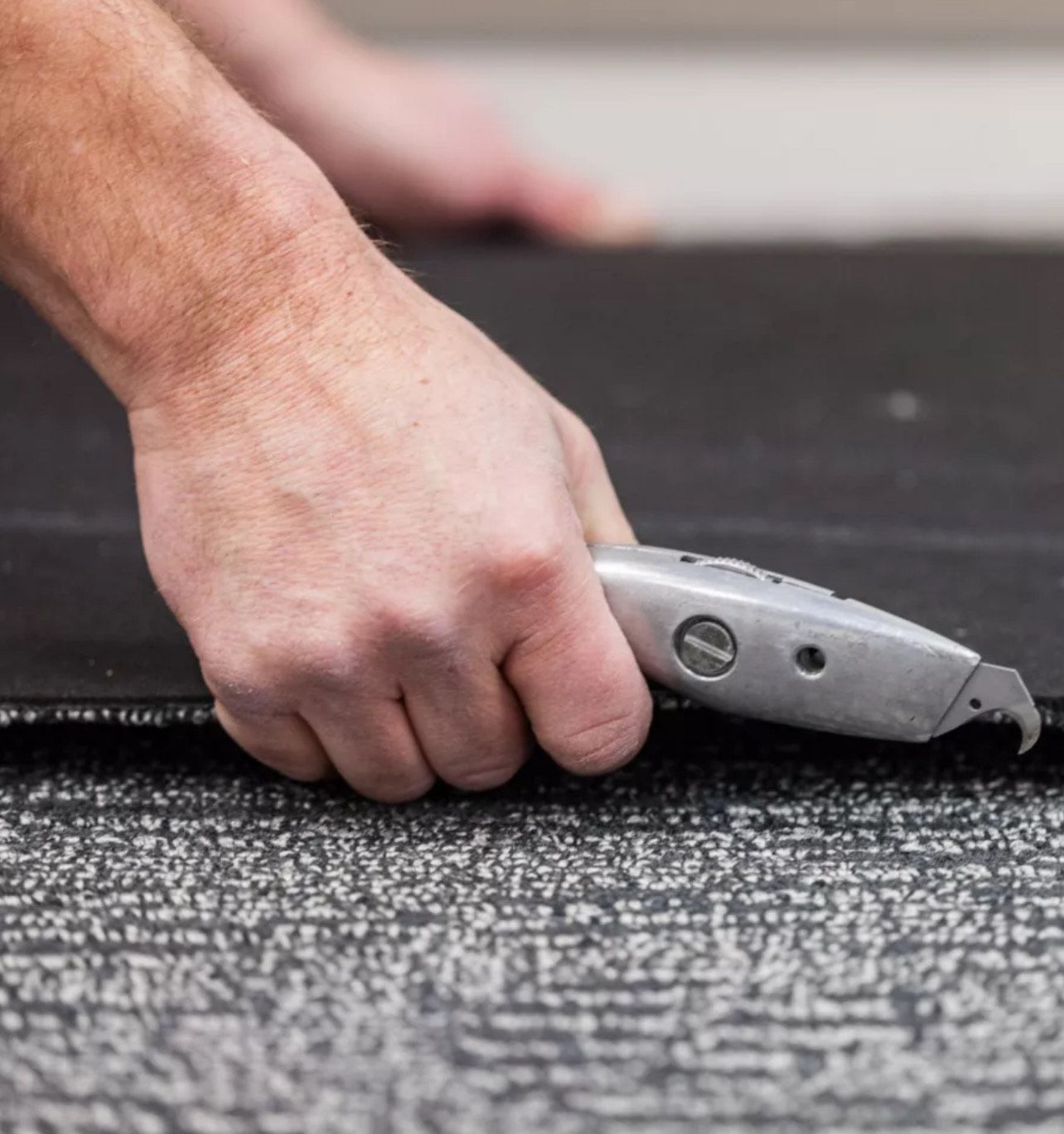 Person cutting dark carpet with a utility knife, close up.