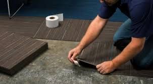 Person kneeling, installing brown floor tiles; toilet paper roll nearby.