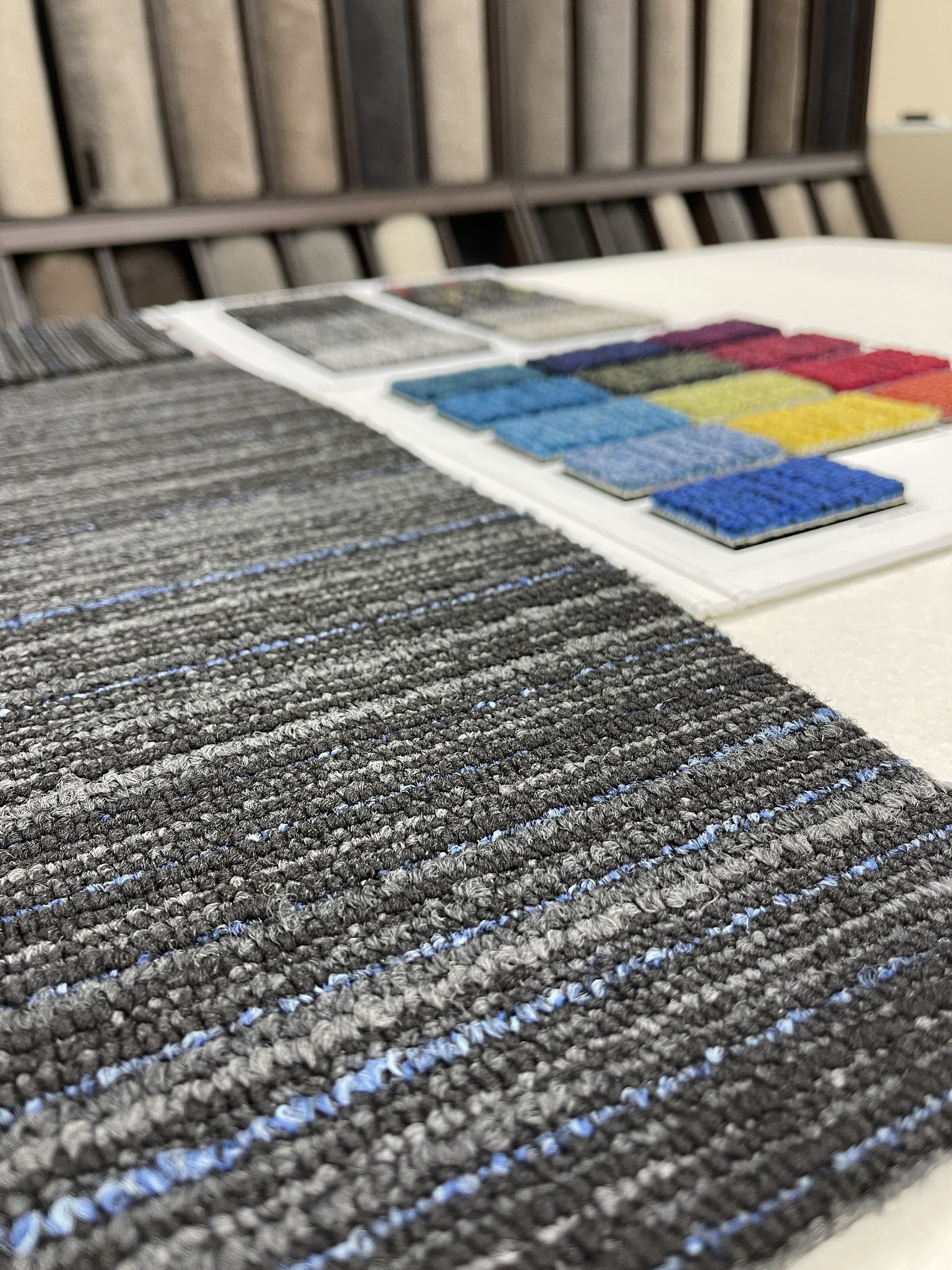 Close-up of a carpet sample showing various blue, grey, and black fibers, with color swatches in the background.
