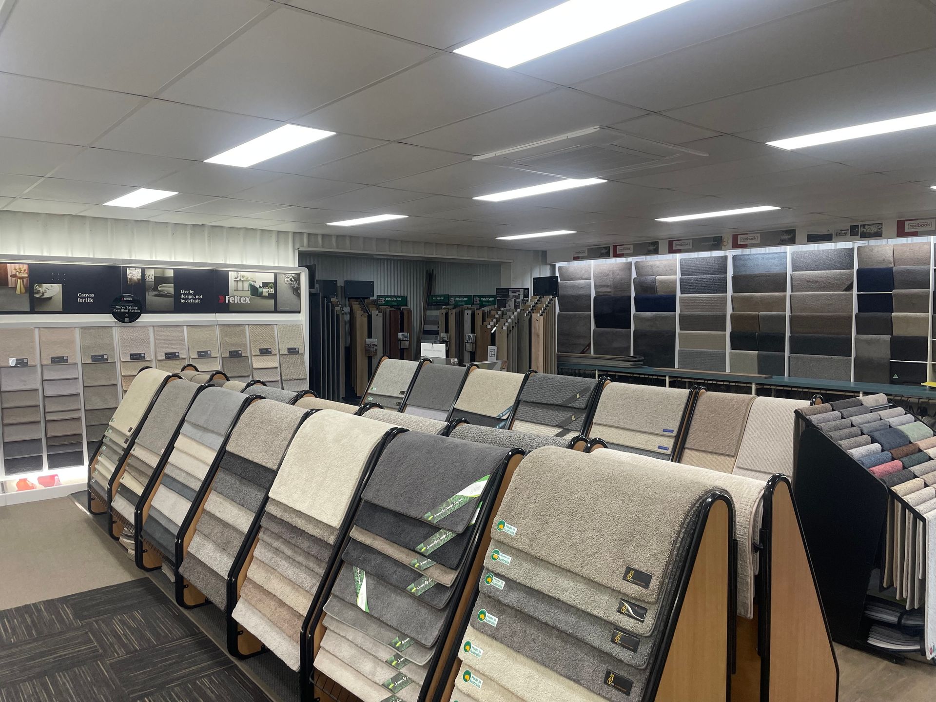 Carpet showroom displaying various samples in neutral colors under bright lights.