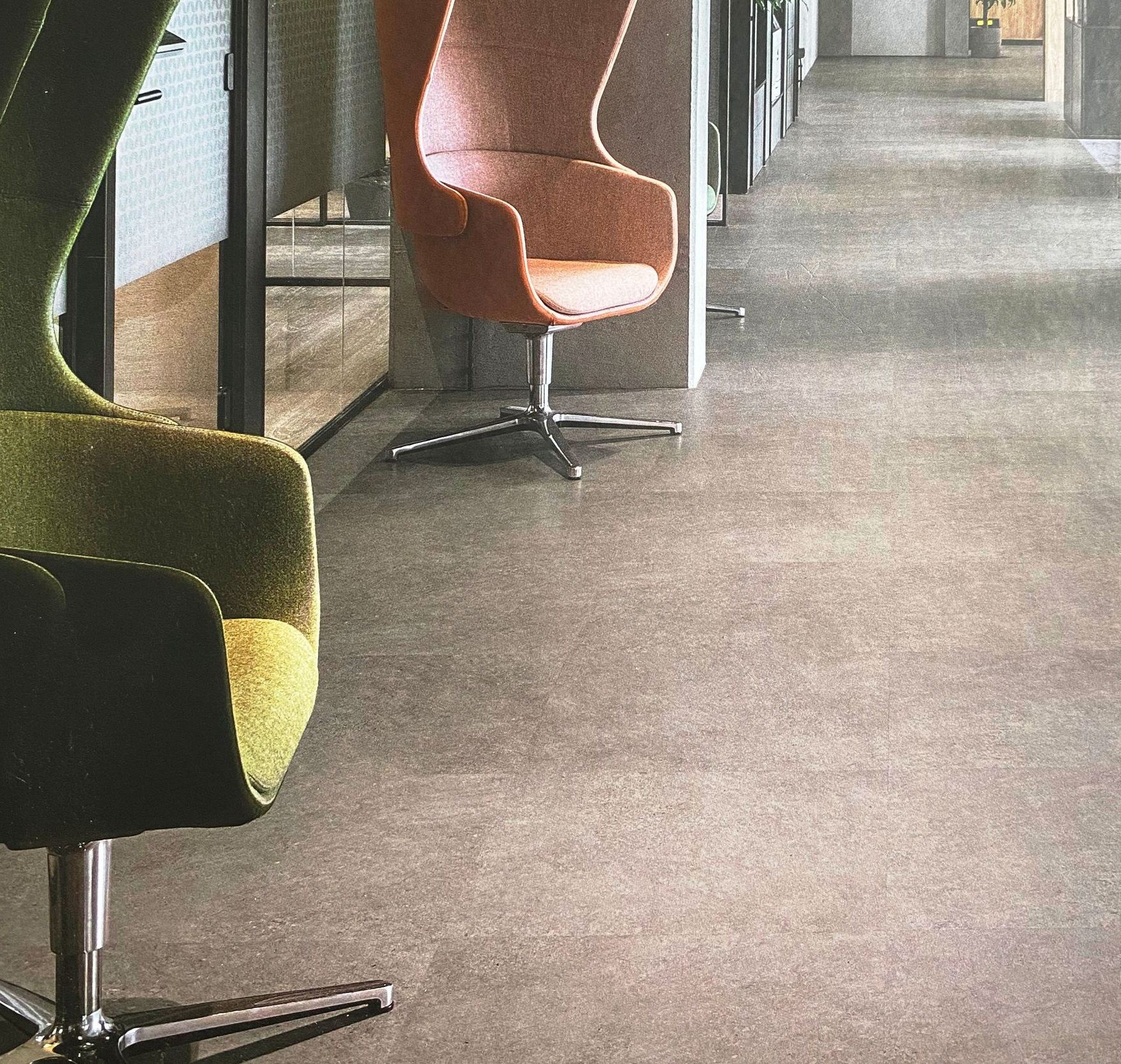 Two swivel chairs in office hallway: green and orange chairs on gray floor.