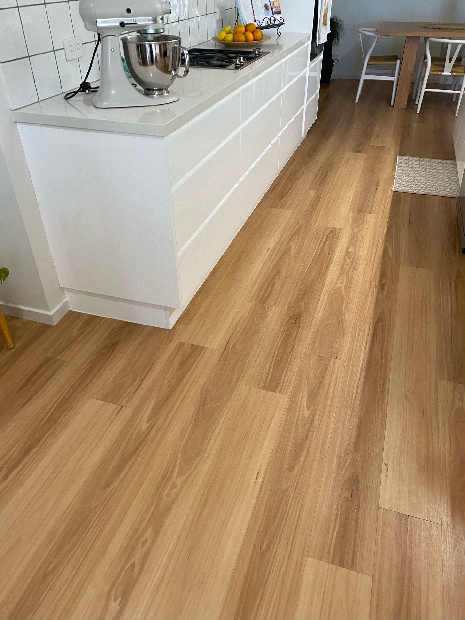 Light wood-look flooring in a kitchen, with white cabinetry and a countertop.