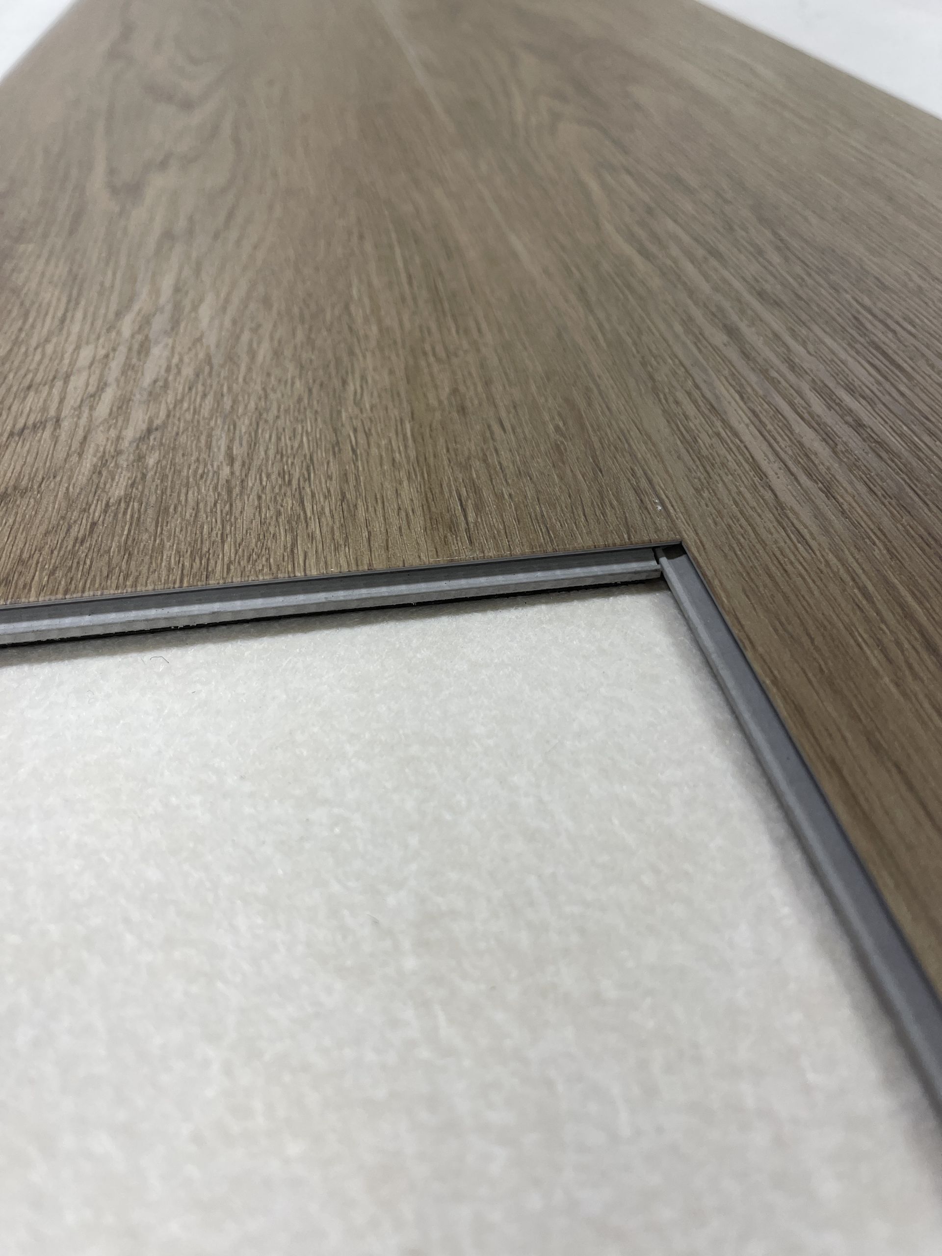 Close-up of interlocking wood-look flooring planks in shades of brown and gray, showing the connecting edge.