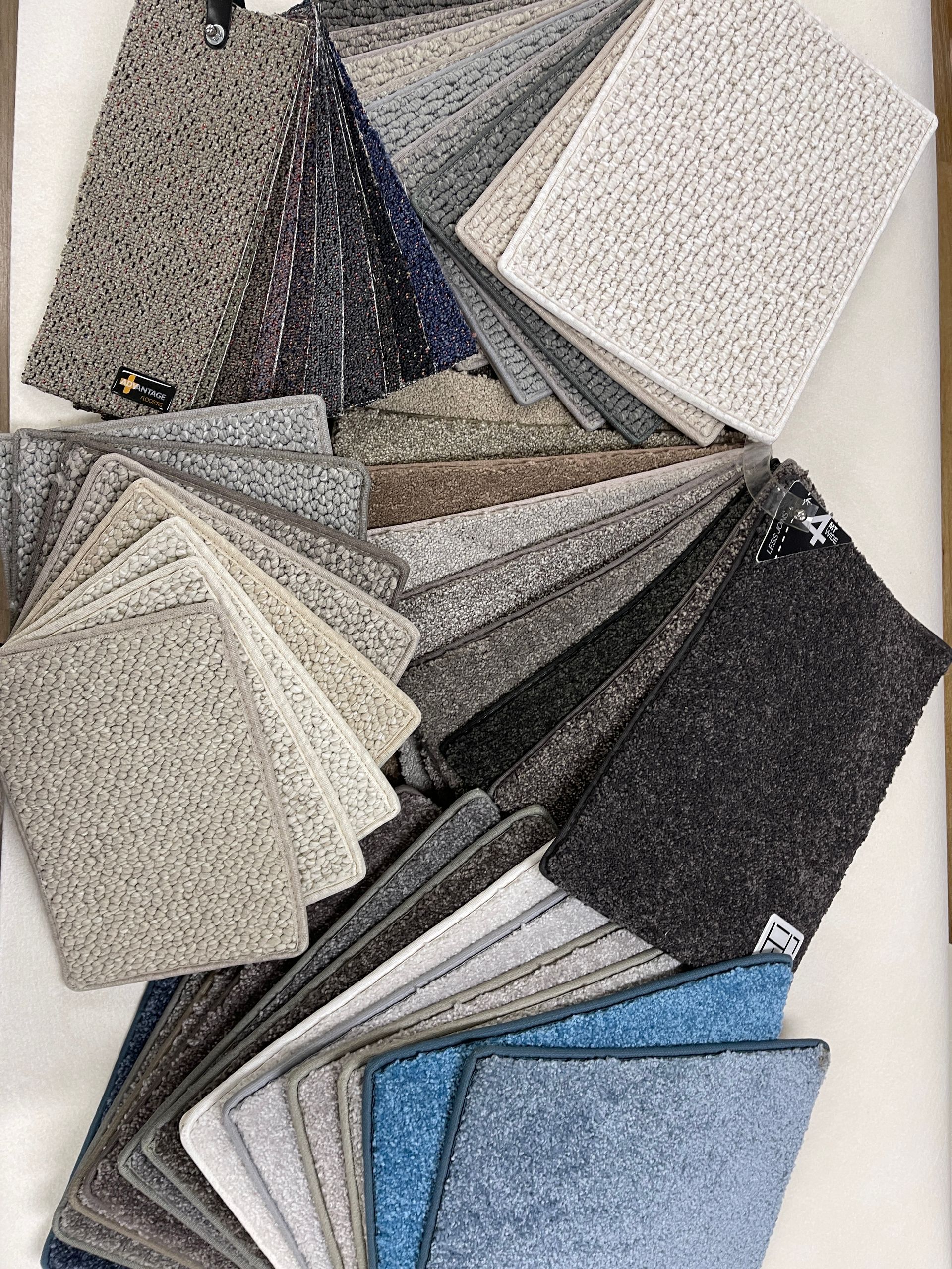 Carpet samples fanned out, showcasing various textures and shades of gray, blue, and neutral tones.