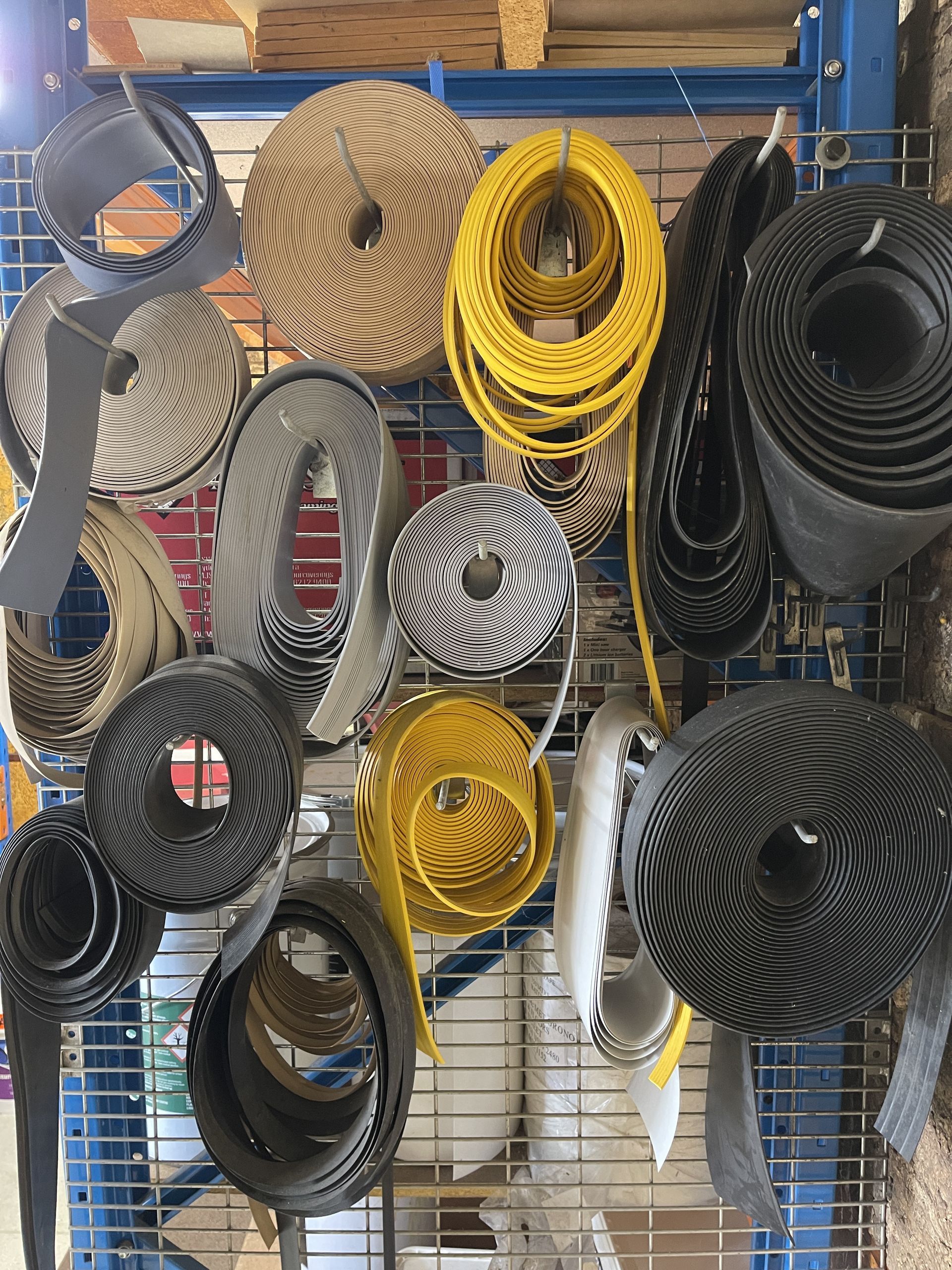 Assortment of coiled decorative trim in yellow, black, white, and gray hanging on a wire rack.