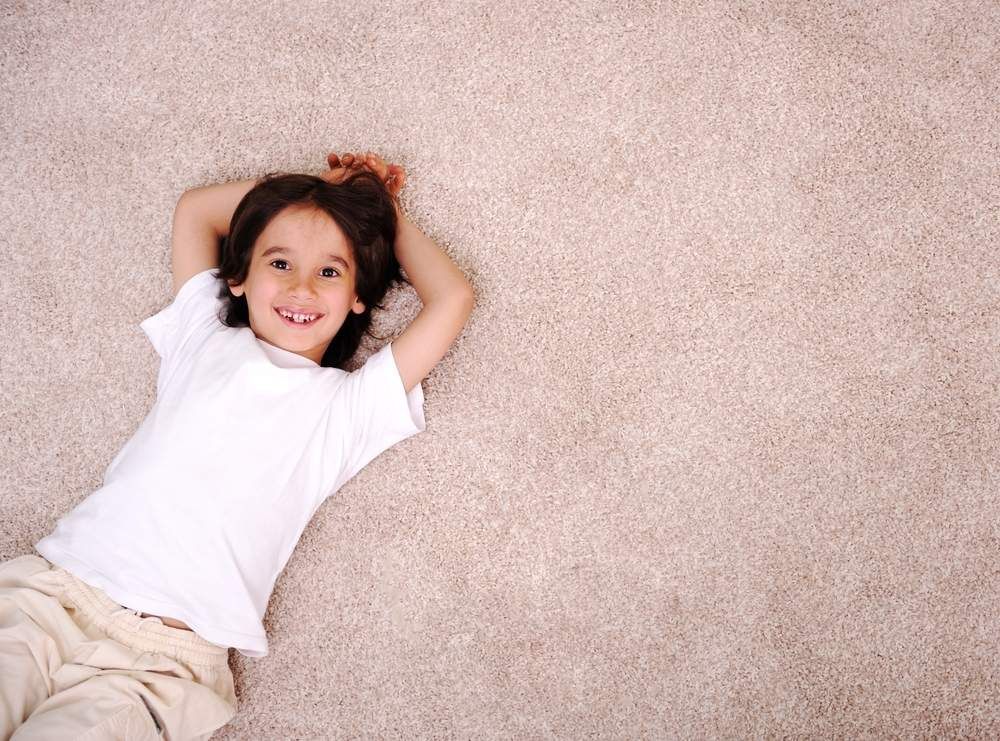 Smiling Child with Dark Hair Lying on Beige Carpet — Gava Floor Centre in Casino, NSW