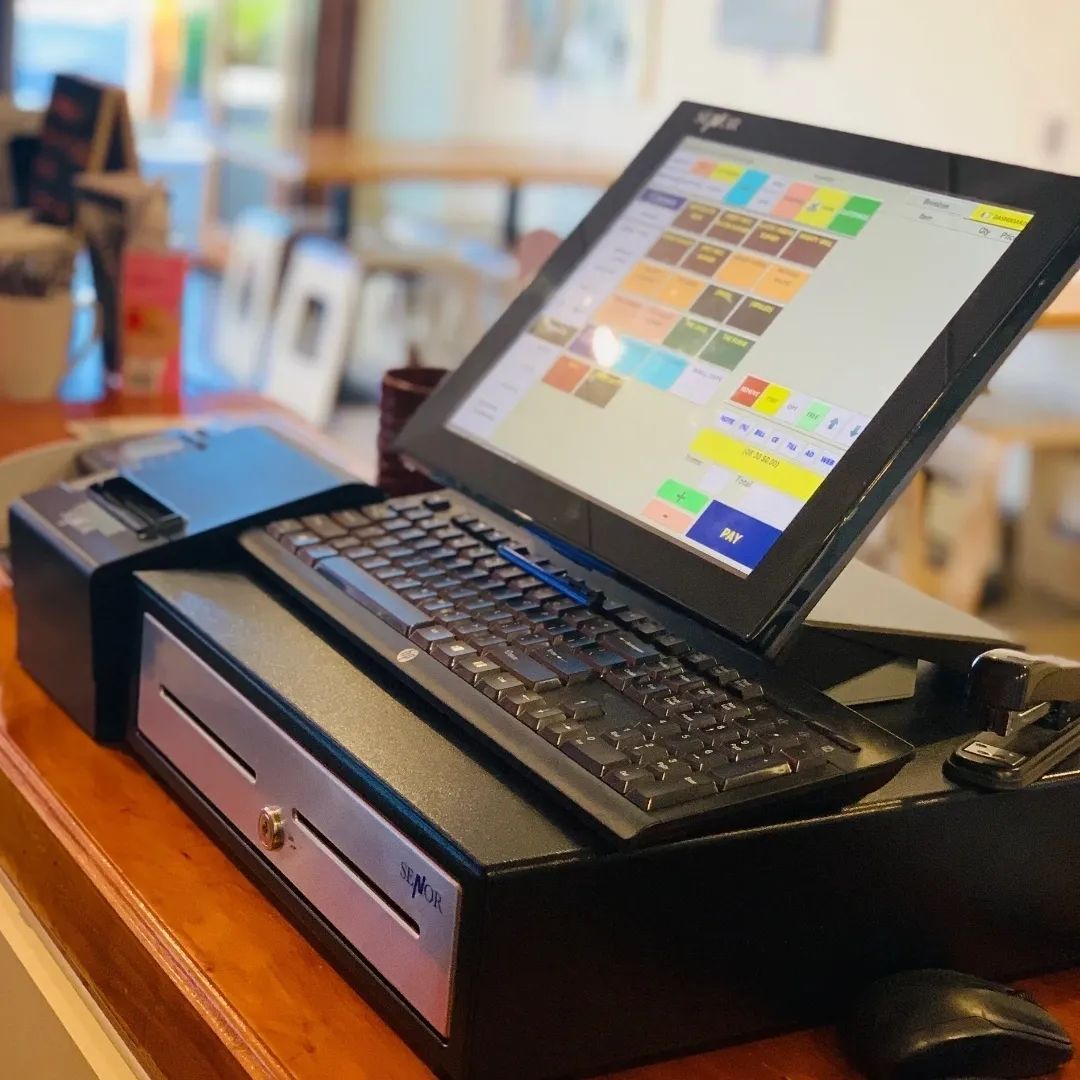 Point-of-sale system on a wooden counter: monitor, keyboard, cash drawer, and receipt printer.