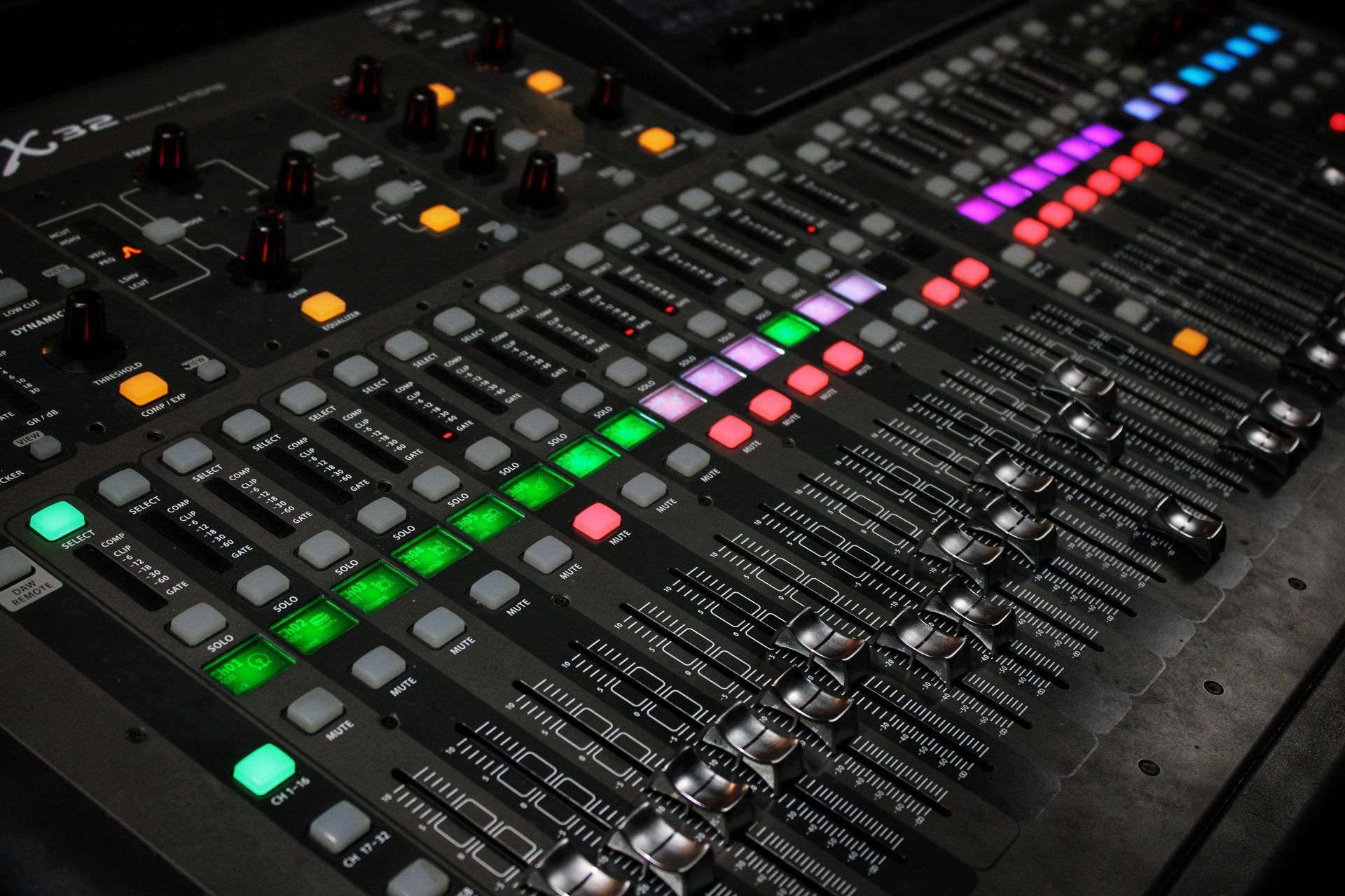 Close-up of a digital audio mixer with illuminated faders and knobs, likely in a recording studio or live sound environment.