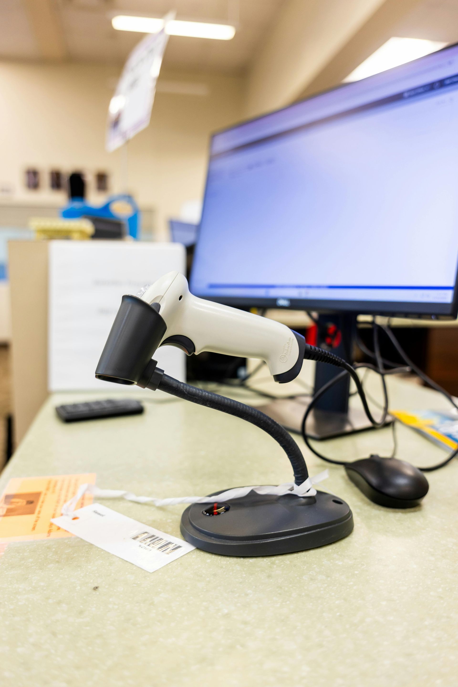 Barcode scanner on a desk, near a computer monitor, with a white and black color scheme.