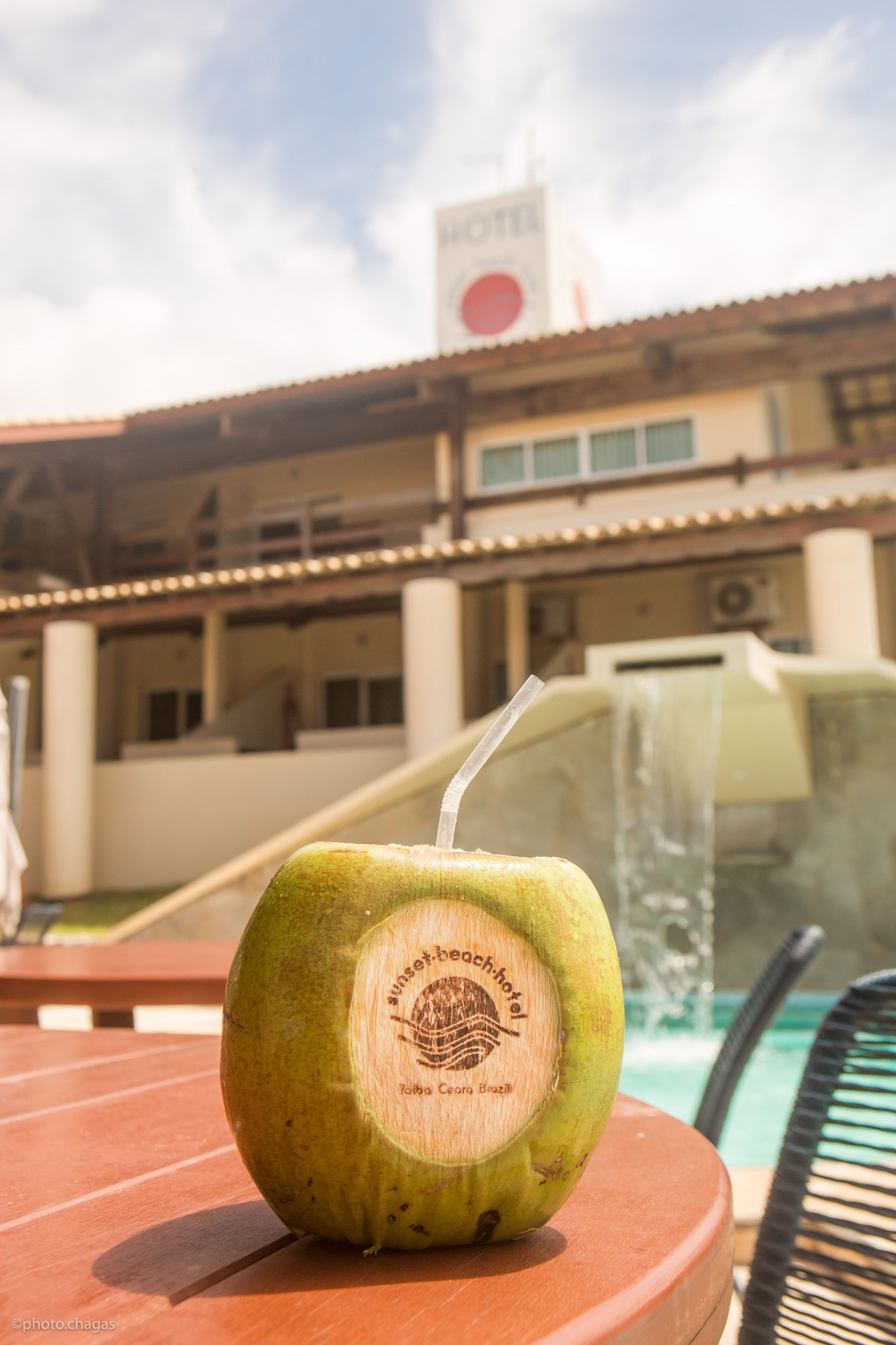 Coconut drink on a table near a pool with a hotel in the background.