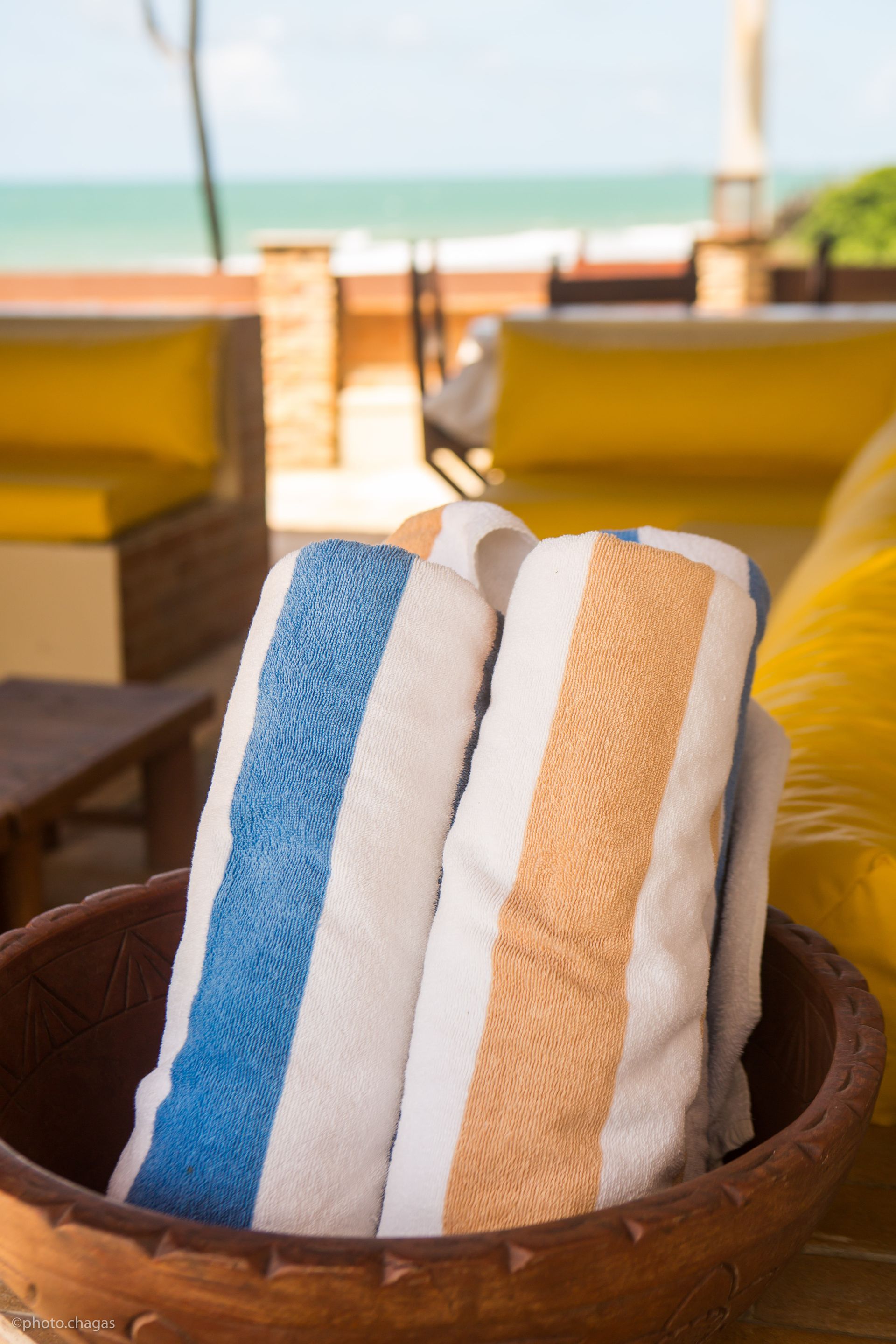 Rolled striped beach towels in a wooden bowl, blurred beach background.