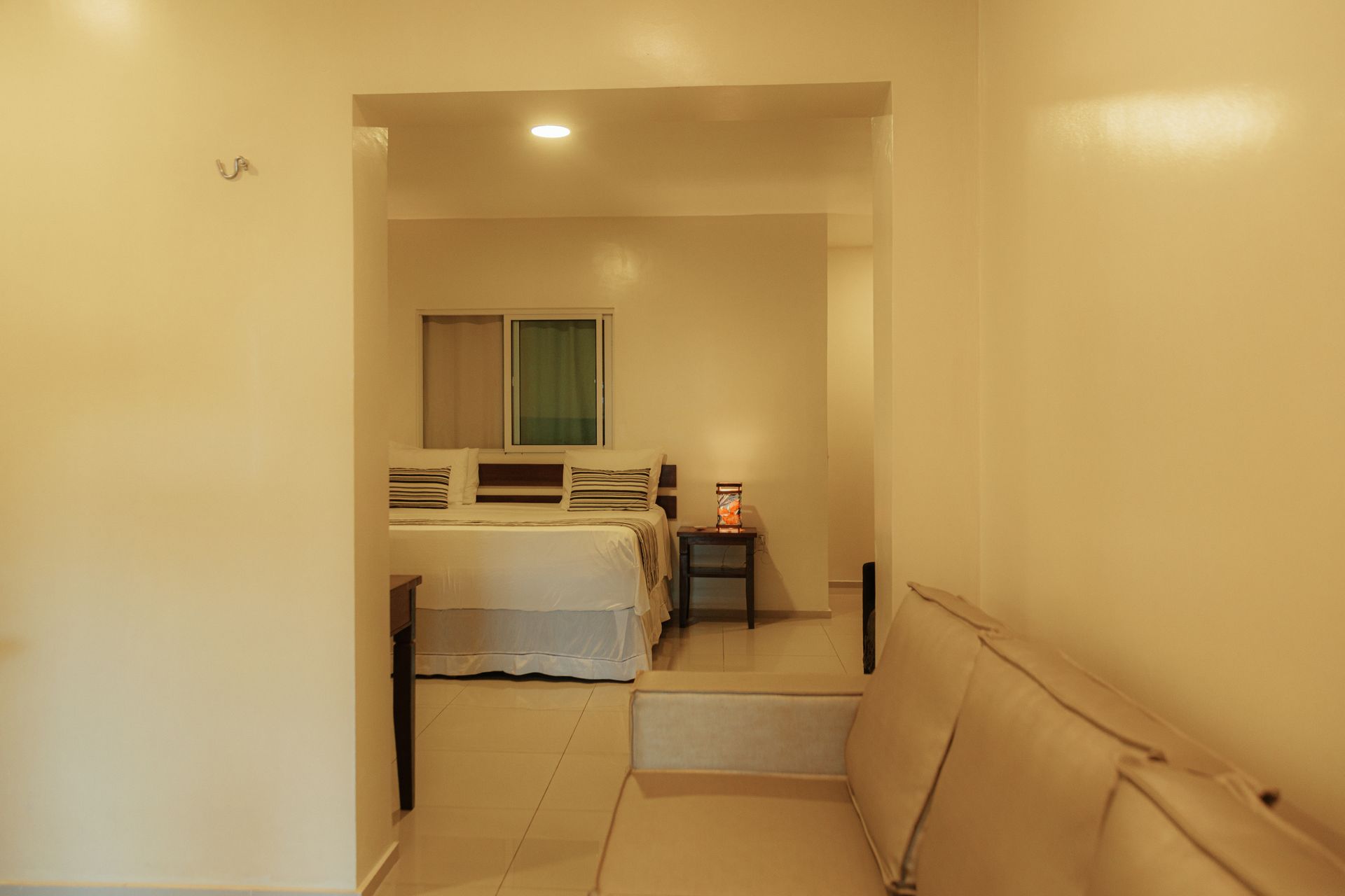 Room interior with arched doorway revealing a bed, windows, and side table. Bright white walls.