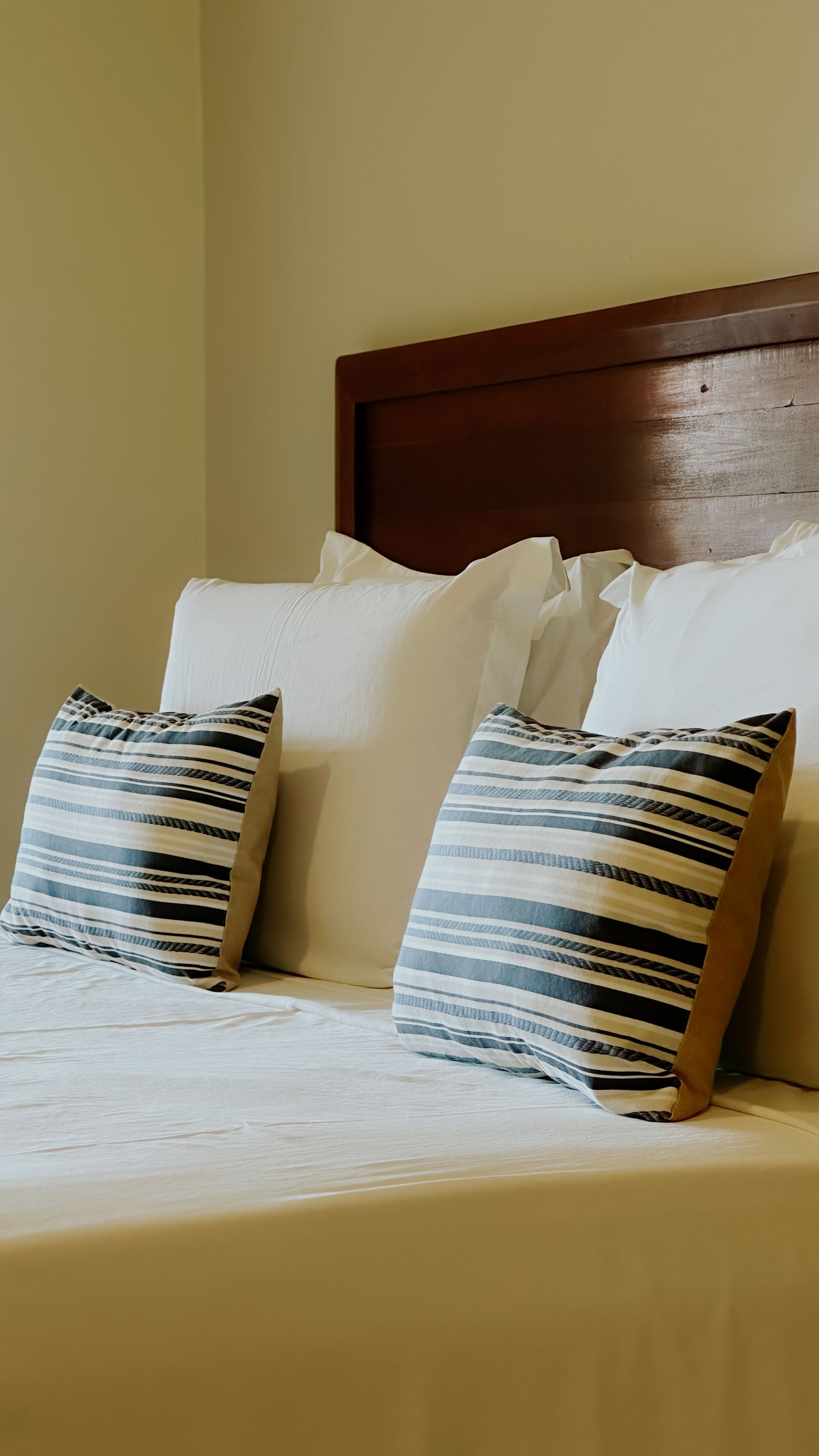 Bed with white bedding, brown headboard, and two patterned throw pillows.