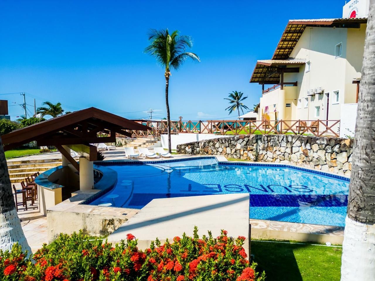 Poolside resort with a pool and ocean view. Sunny day, blue sky, palm tree.