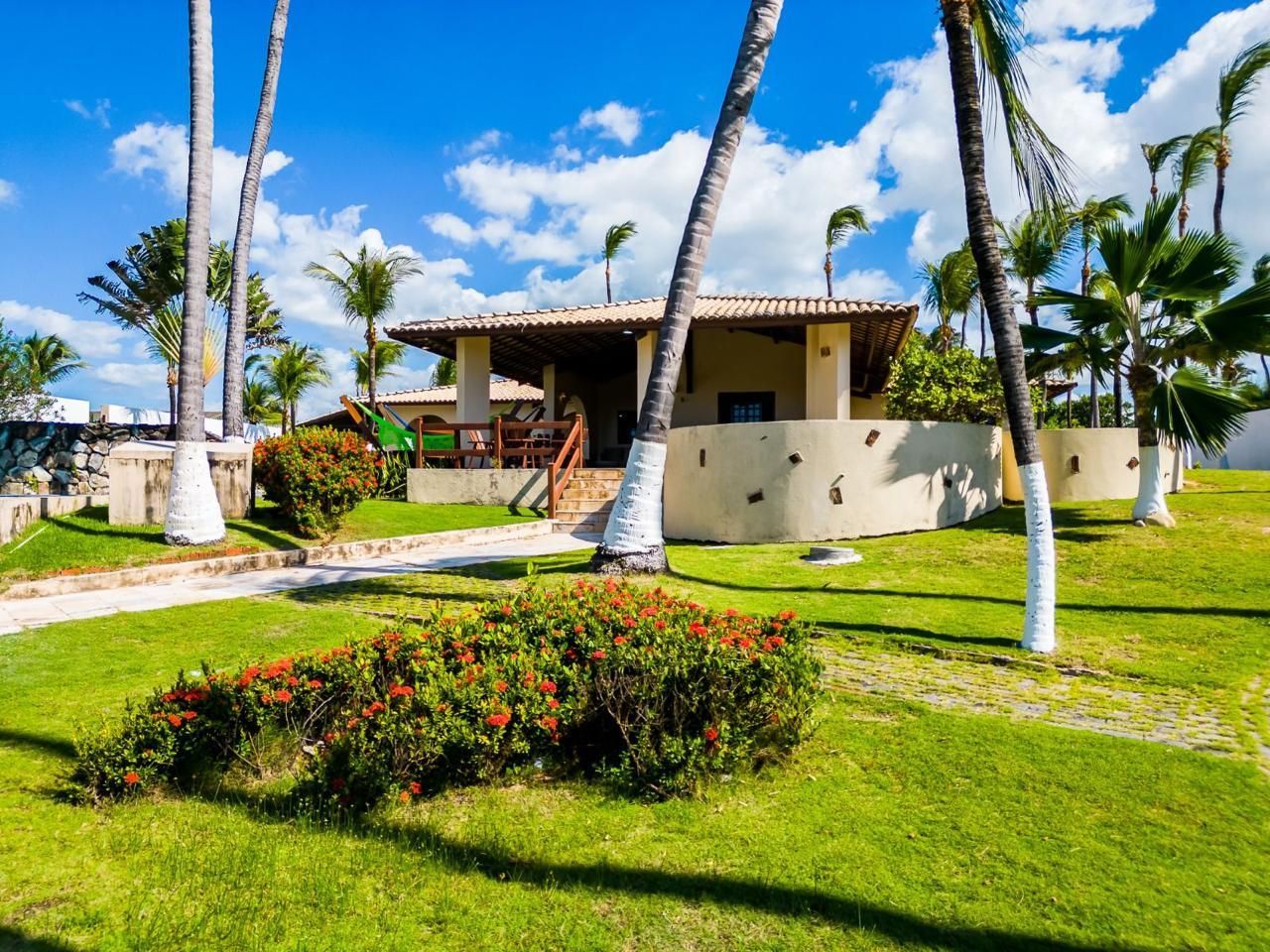 A tropical bungalow with palm trees and a green lawn under a blue sky.