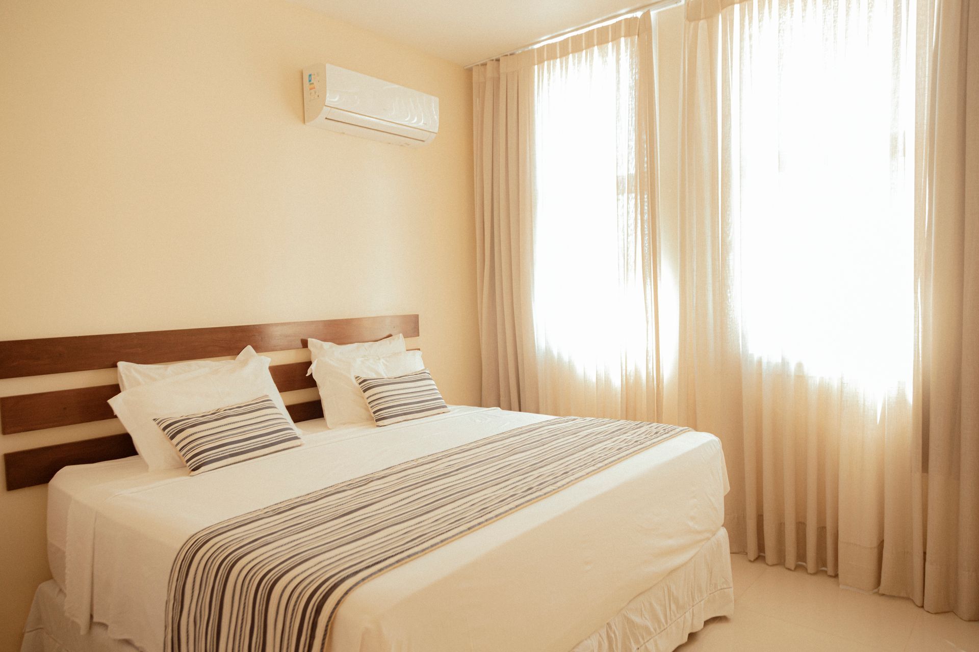 Bedroom with a bed, white bedding, beige walls, and light curtains.