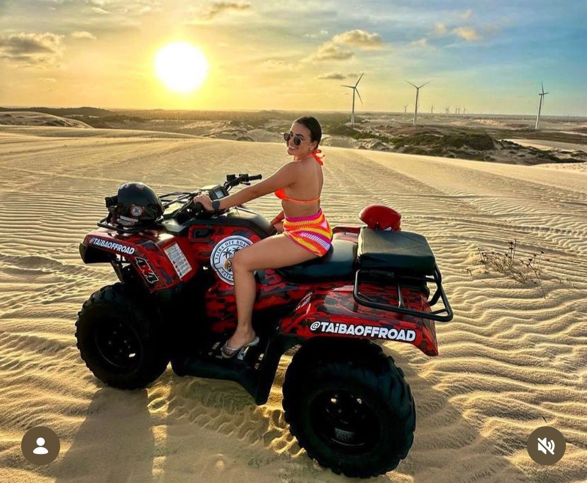 Woman on an ATV in sand dunes at sunset.