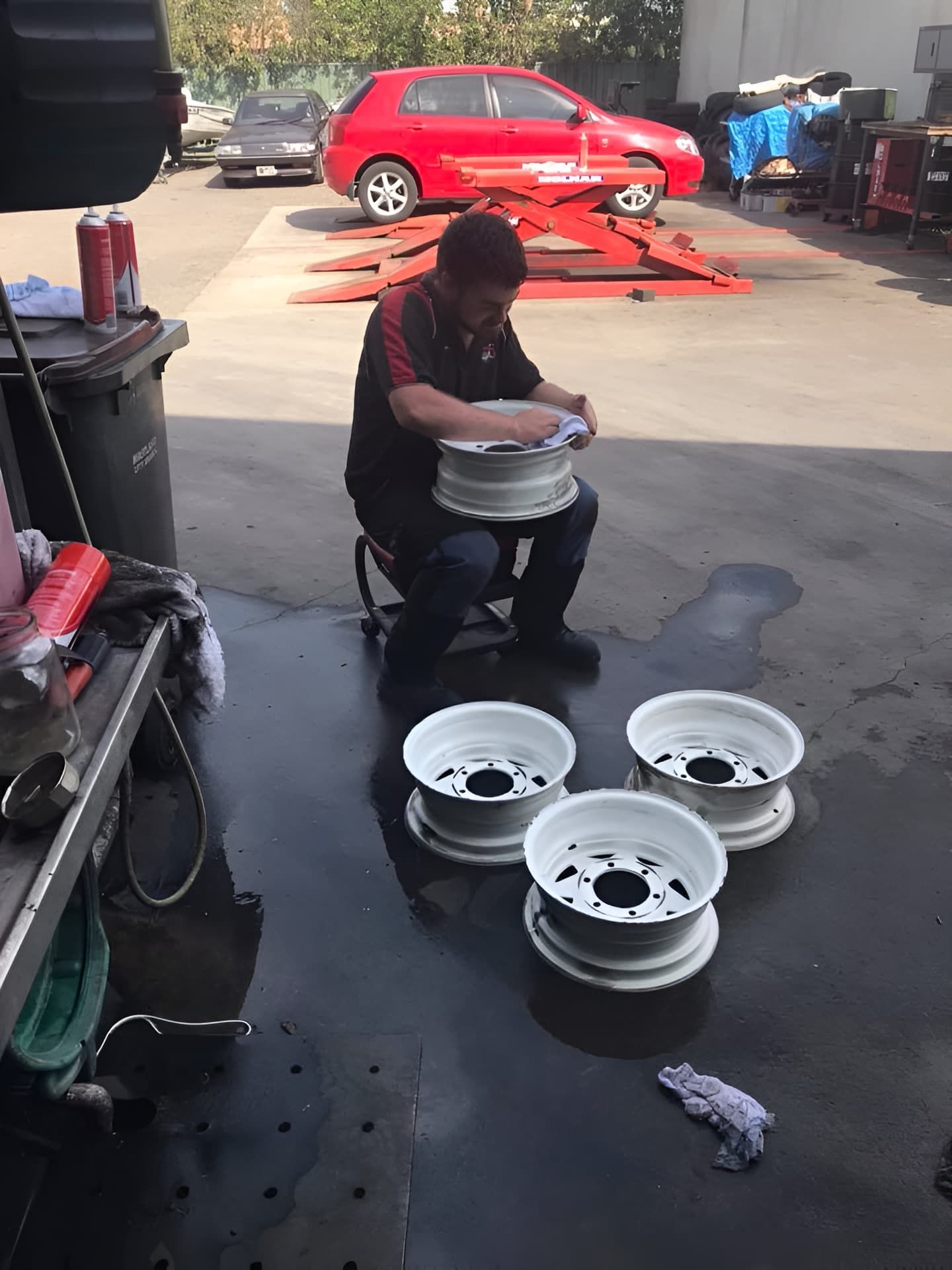 A Man Is Sitting On A Stool In A Garage Working On Wheels — Cannon Automotive Services In East Maitland, NSW
