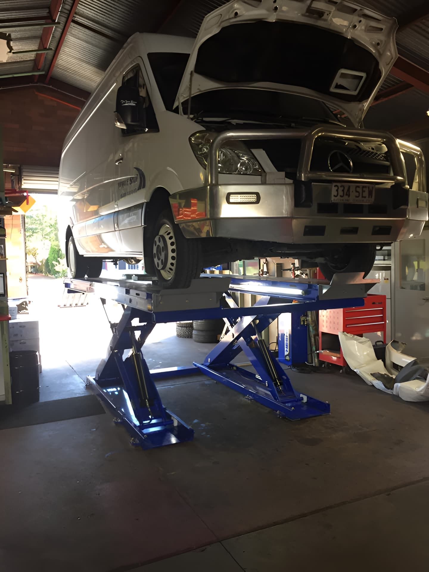 A White Van Is Sitting On Top Of A Lift In A Garage — Cannon Automotive Services In East Maitland, NSW