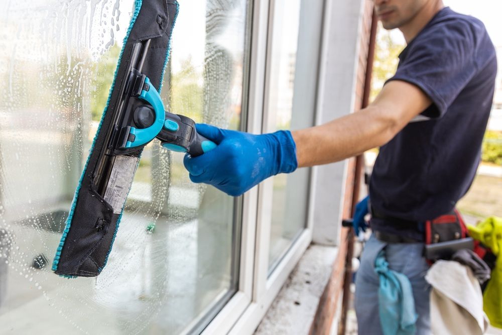 Person in blue gloves using a squeegee to clean a window.