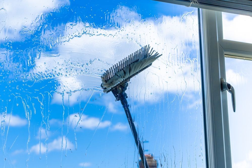 A window being cleaned with a long-handled brush against a blue sky with clouds.
