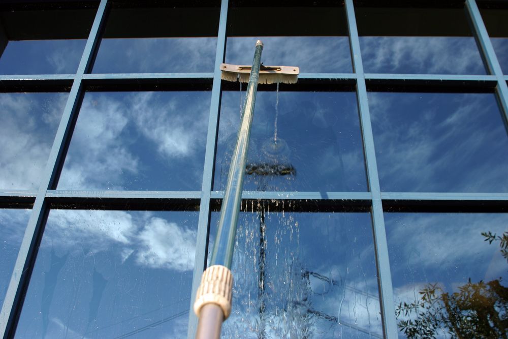 Window being cleaned with a long-handled squeegee, reflecting a cloudy blue sky.