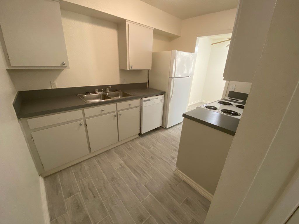 A kitchen with white cabinets , a refrigerator , stove , sink and dishwasher.