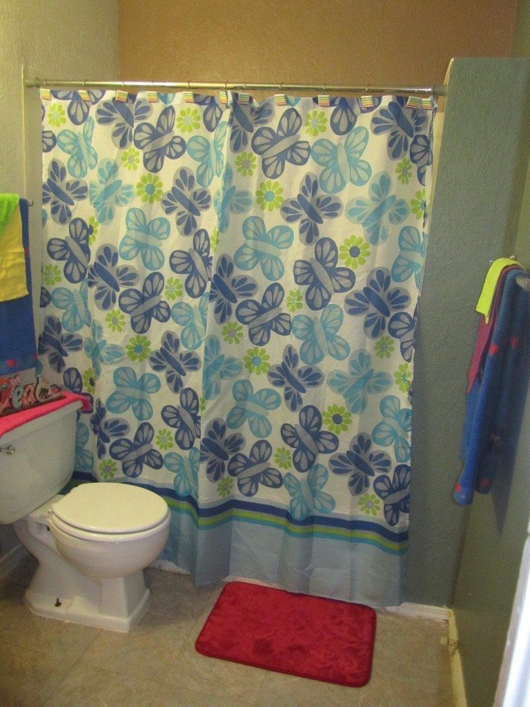 A bathroom with a toilet a shower curtain and a rug