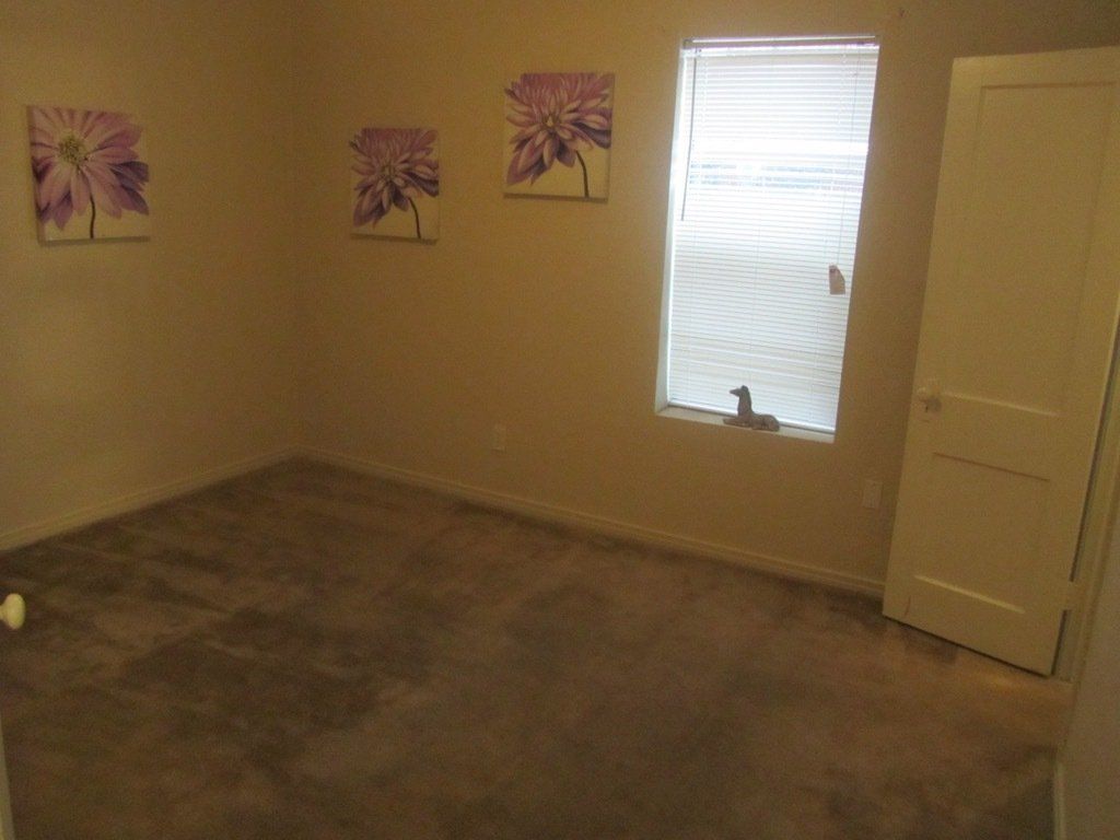 An empty bedroom with three paintings on the wall and a window.