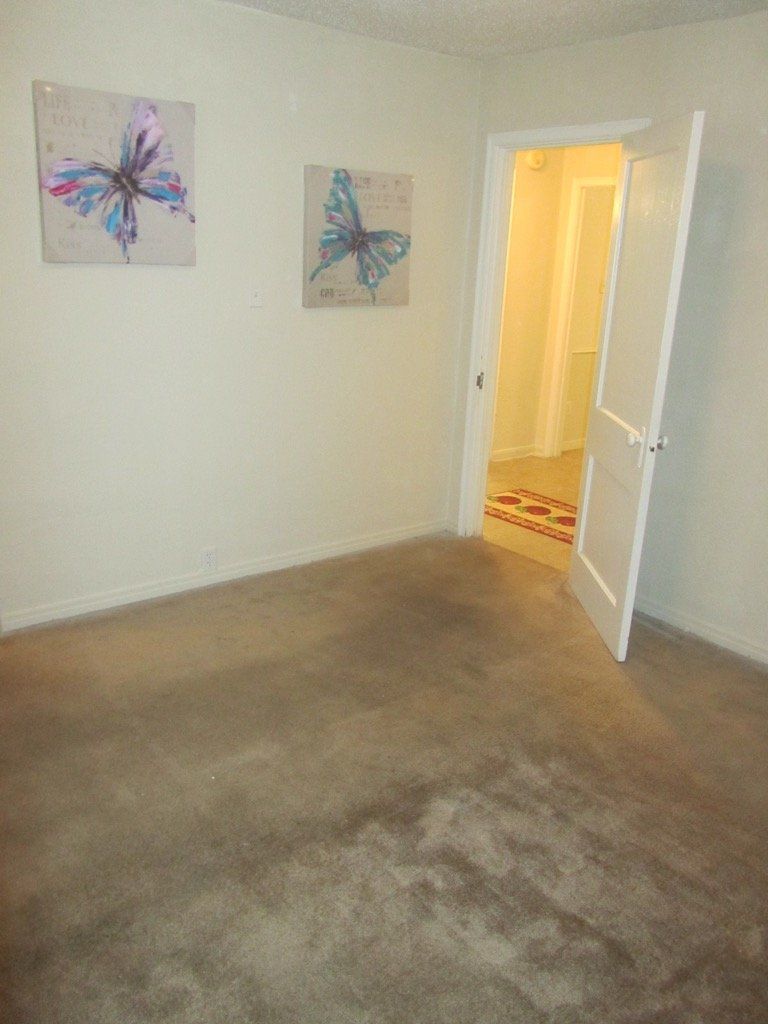 A bedroom with a carpeted floor and two paintings on the wall.
