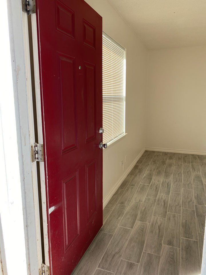 A red door is open in an empty room with a window.