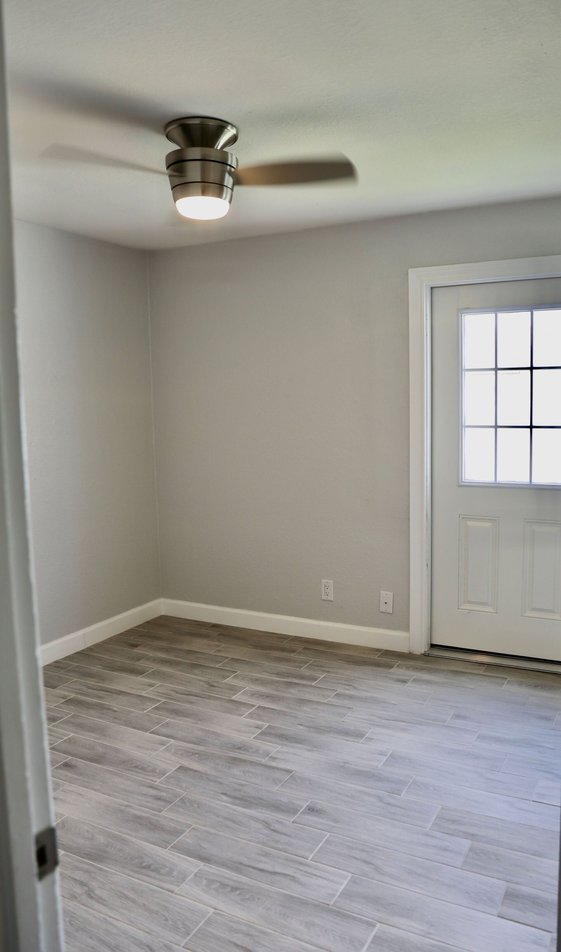 An empty room with a ceiling fan and a window.